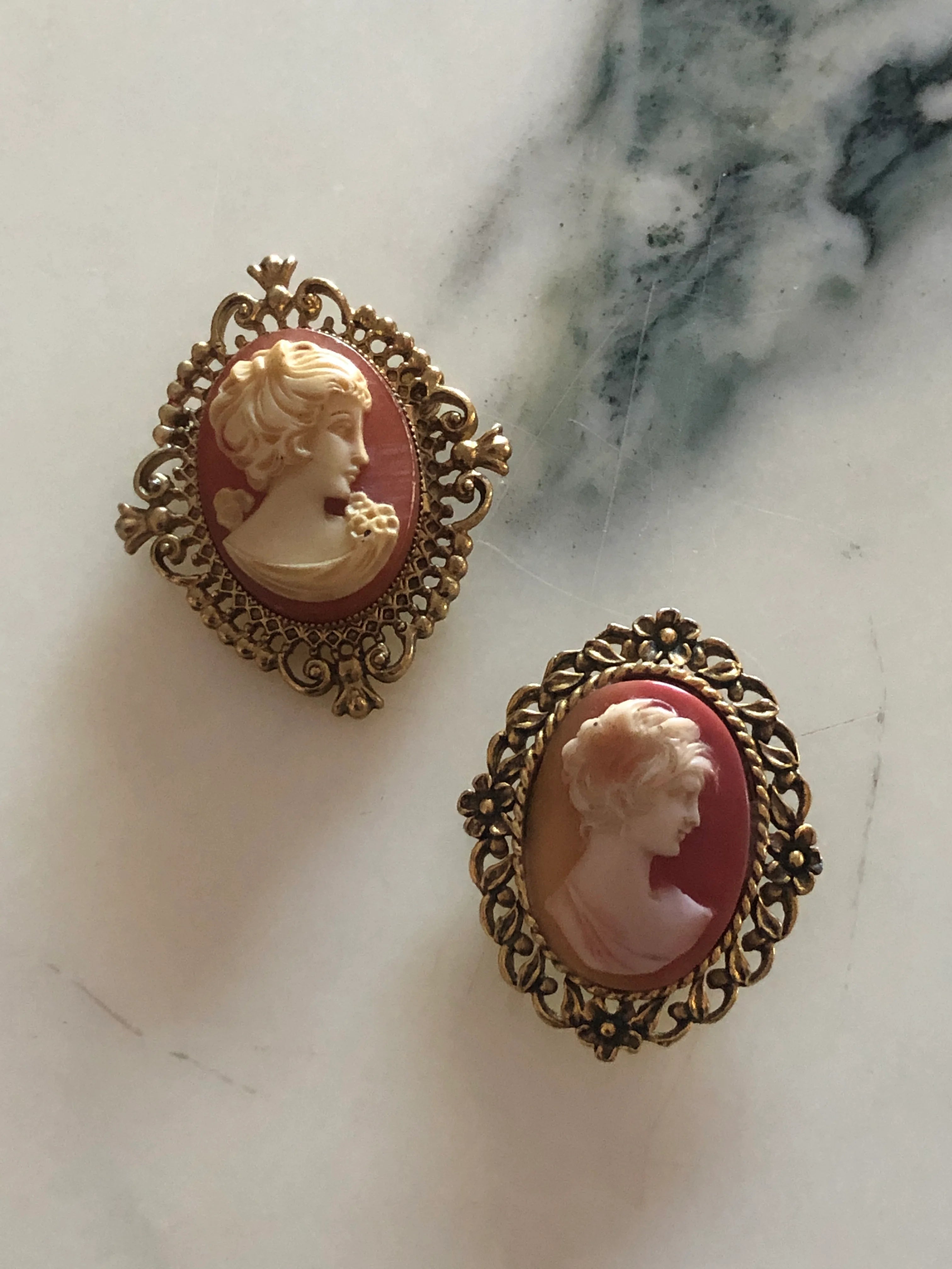 Two Broochella Duo Sorelle vintage cameo brooches on a marble surface