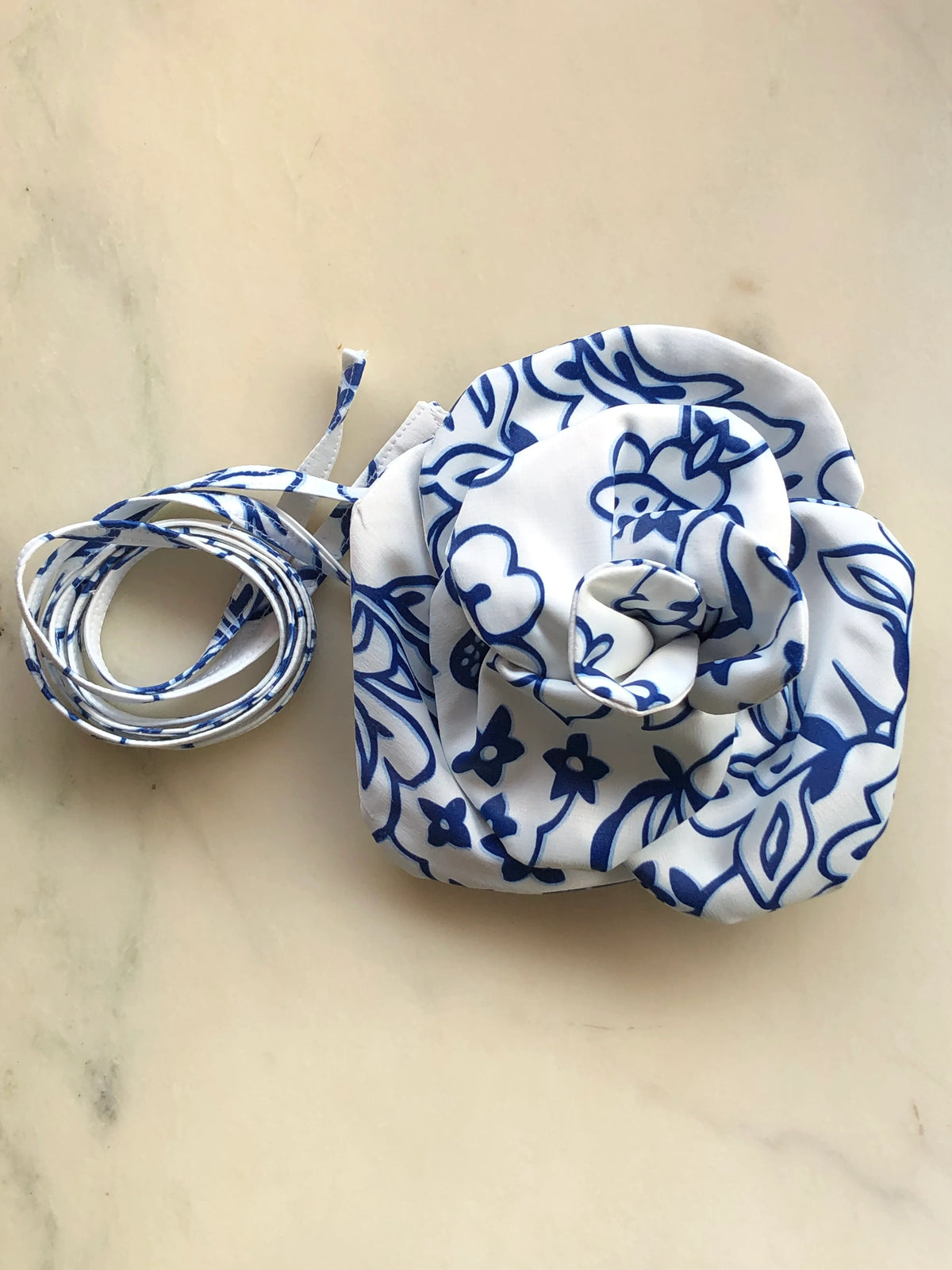 Broochella Electra Floral Brooch or Choker in white with cobalt blue floral print, featuring an oversized sculptural flower and matching tie, photographed on a marble background.