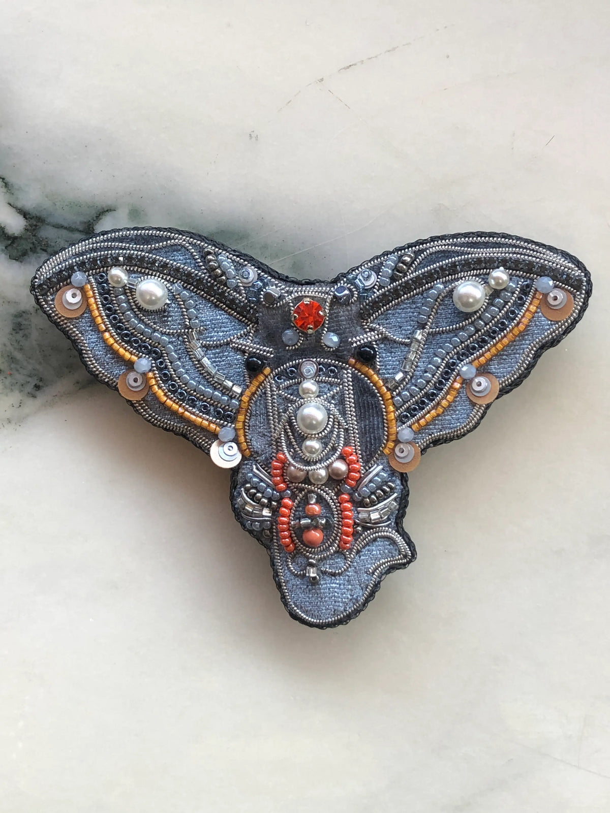 Broochella Elephant Face Brooch hand embellished with silver, grey, orange and pearl beads, crystals and sequins, photographed on white marble.