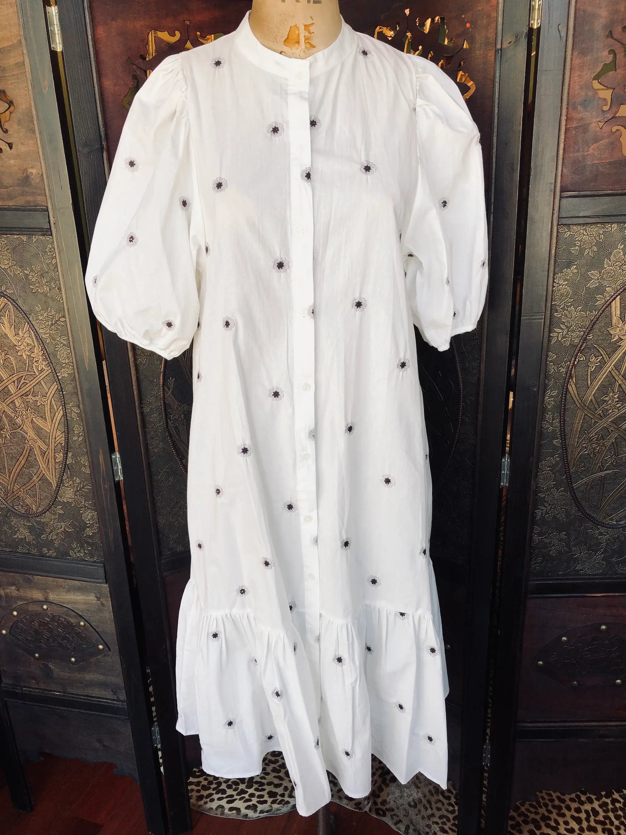Broochella size small, white cotton shirt dress with embroidered flowers on a mannequin against a decorative wooden background