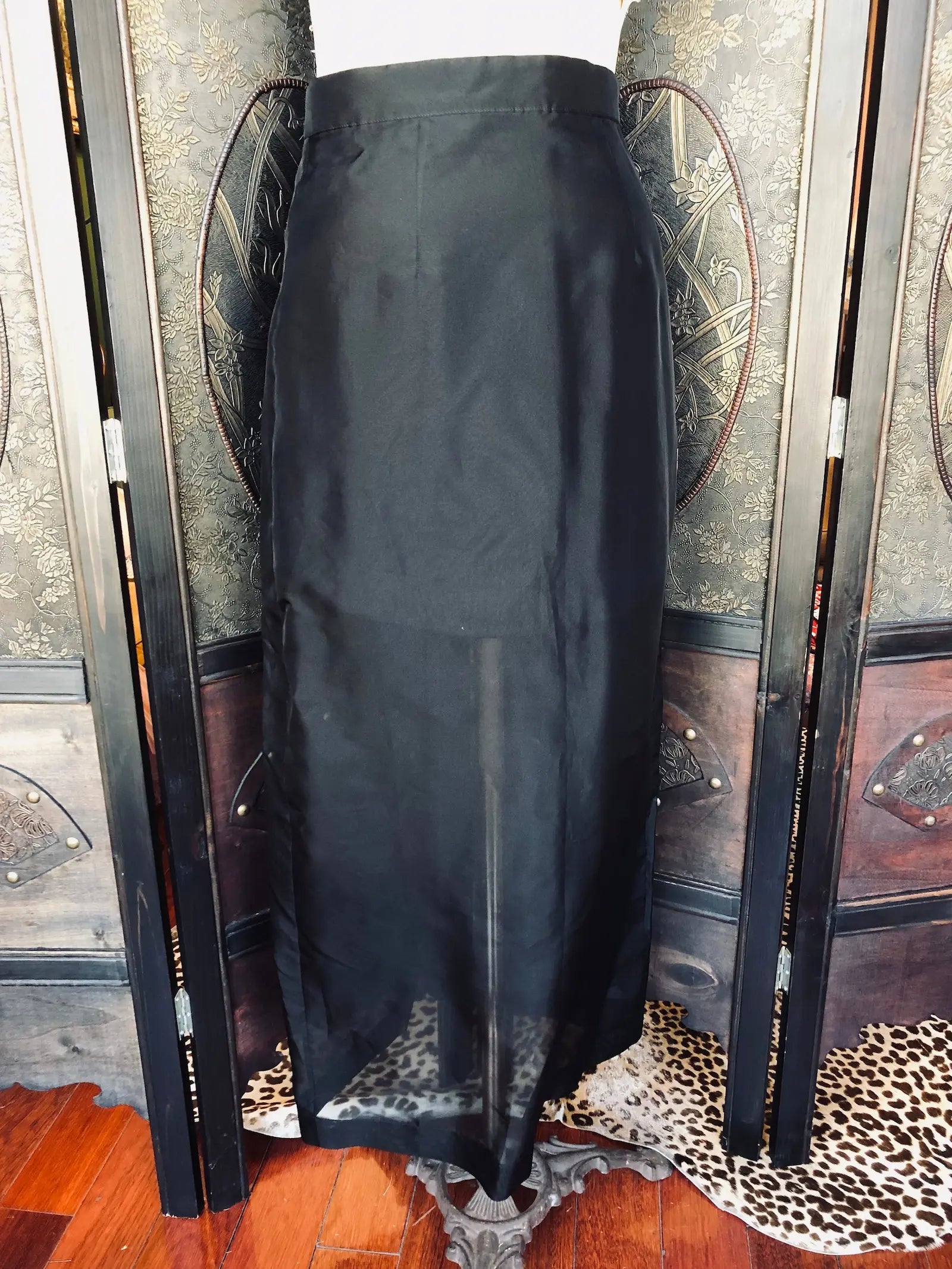 Broochella Emerson Studios black, silk organza maxi skirt in size small. It is presented on a vintage mannequin. The background is an ornate, dark wood room divider. 