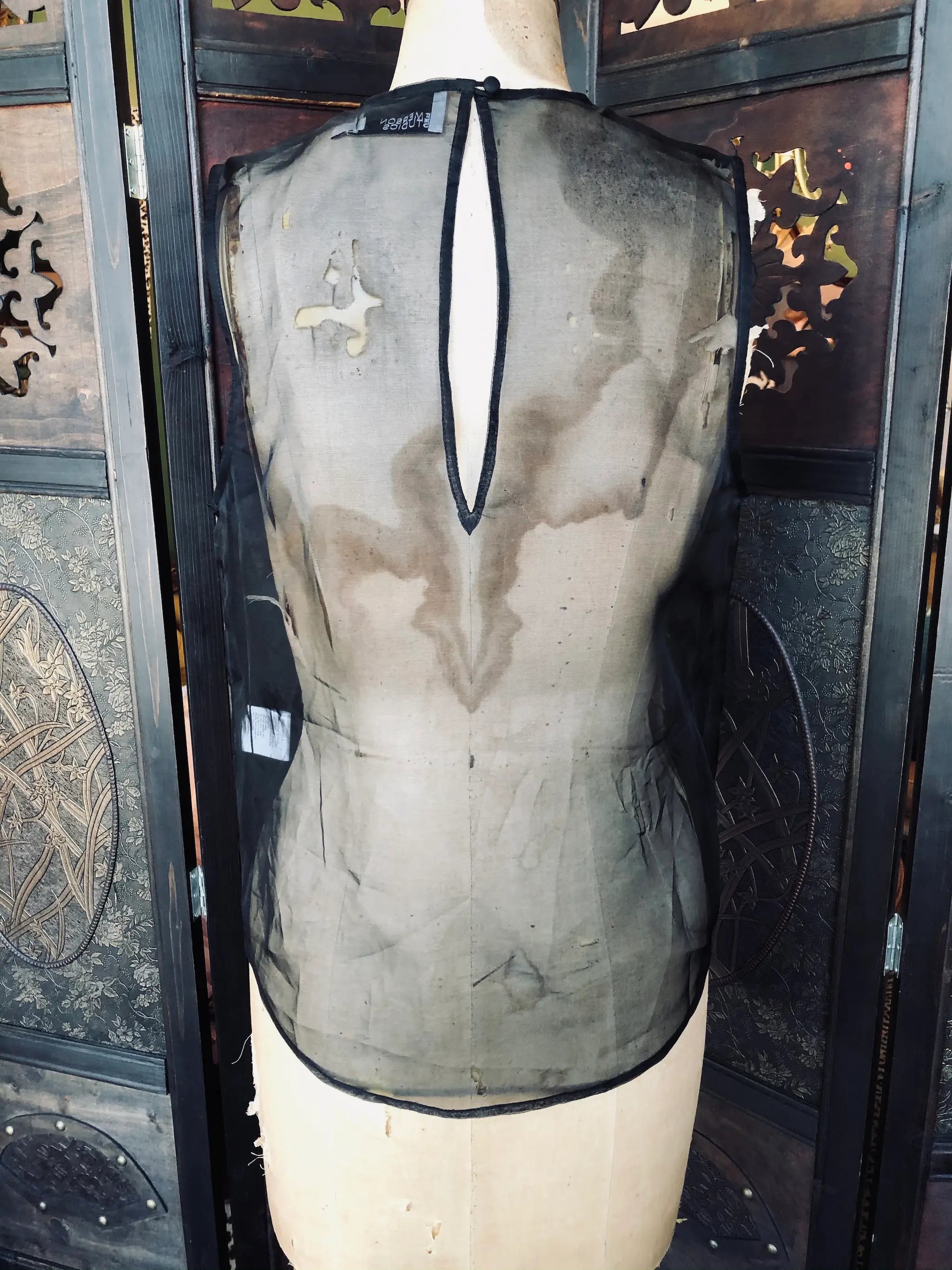 Broochella Emerson studios, Small, 100% Silk, Black, Sleeveless design, Sheer silk finish, Front panel pockets. Keyhole back detail. It is presented on a vintage mannequin. The background is a ornate, vintage, dark wood room divider. 