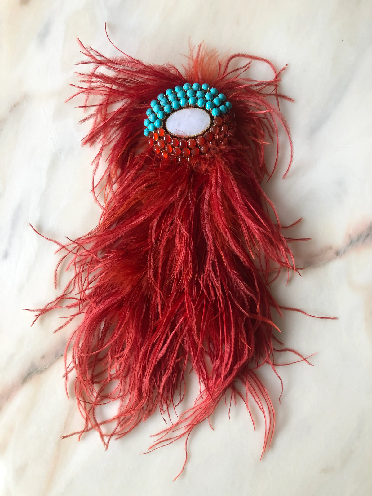 Broochella rust Feather Bejewelled Brooch with cascading ostrich feathers and an ornate turquoise, red and white stone centre, photographed on a white marble background.