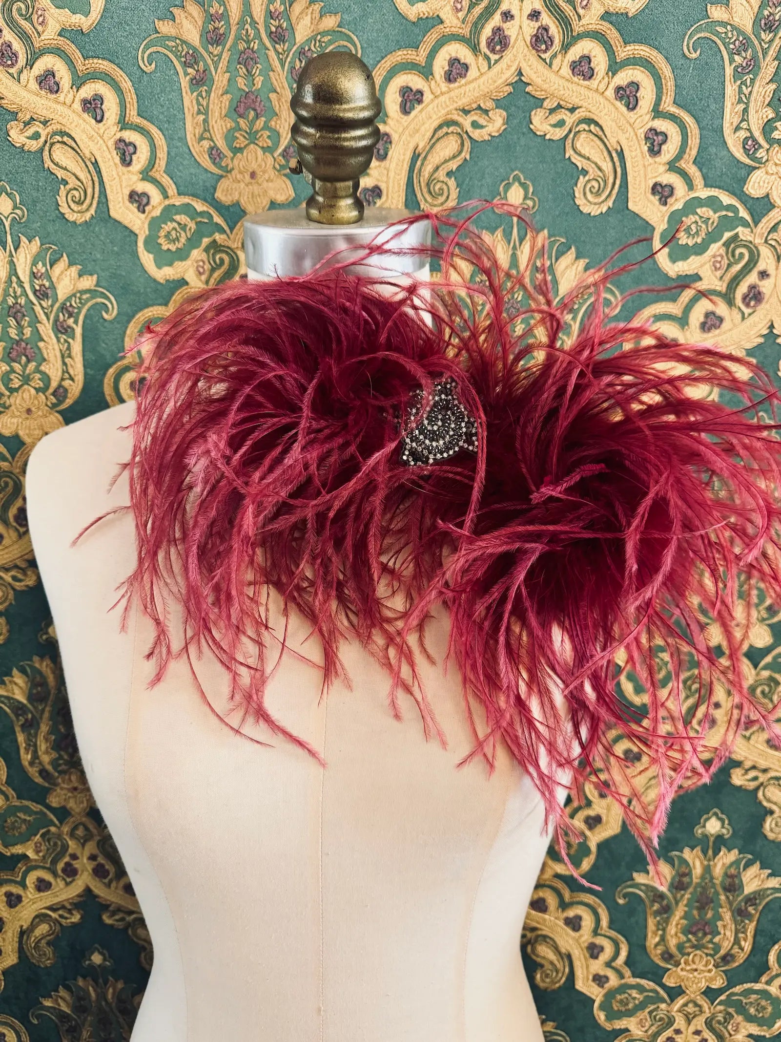 Broochella magenta handmade large feather bow brooch with embellished centre.  Pictured on a mannequin.  The background is green and gold damask wallpaper.