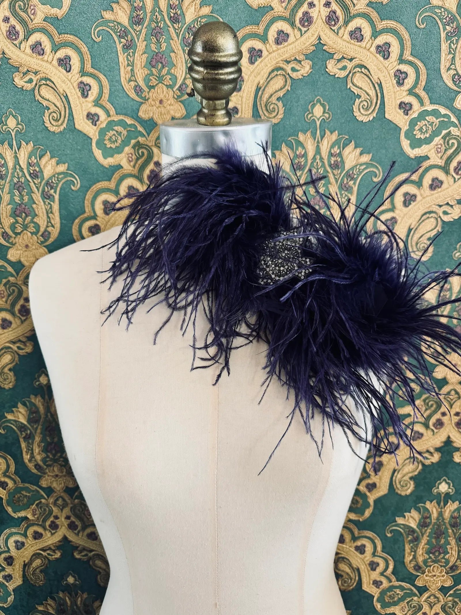 Broochella purple handmade large feather bow brooch with embellished centre.  Pictured on a mannequin.  The background is green and gold damask wallpaper.