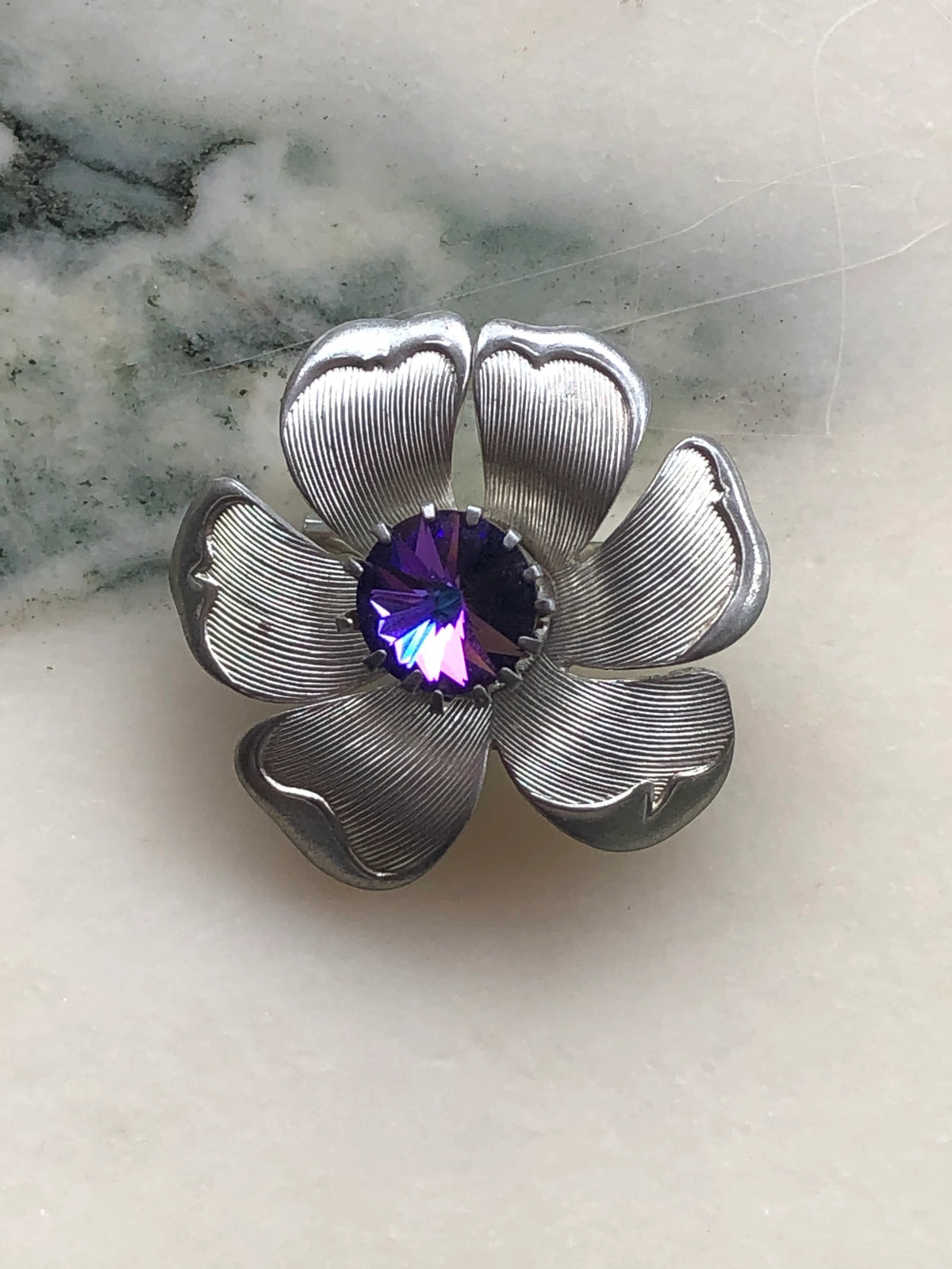 Broochella Fiore Viola Vintage Brooch featuring six sculptural silver-tone textured petals surrounding a large faceted violet purple crystal centre.