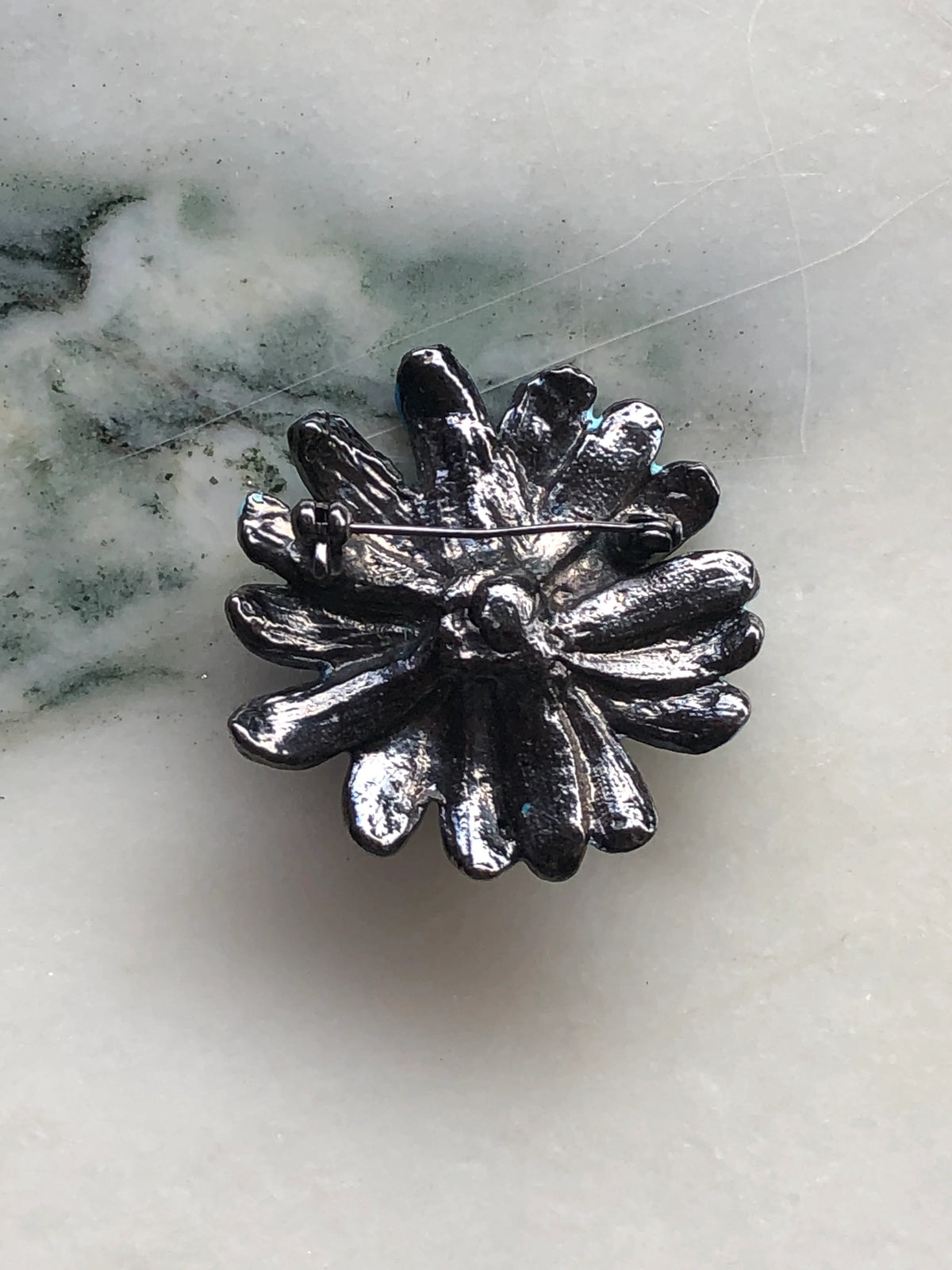 Broochella Fleur de Saphir Vintage Enamel Brooch back view showing the dark silver-tone floral setting and traditional pin fastening, photographed on a white marble background with soft grey-green veining.