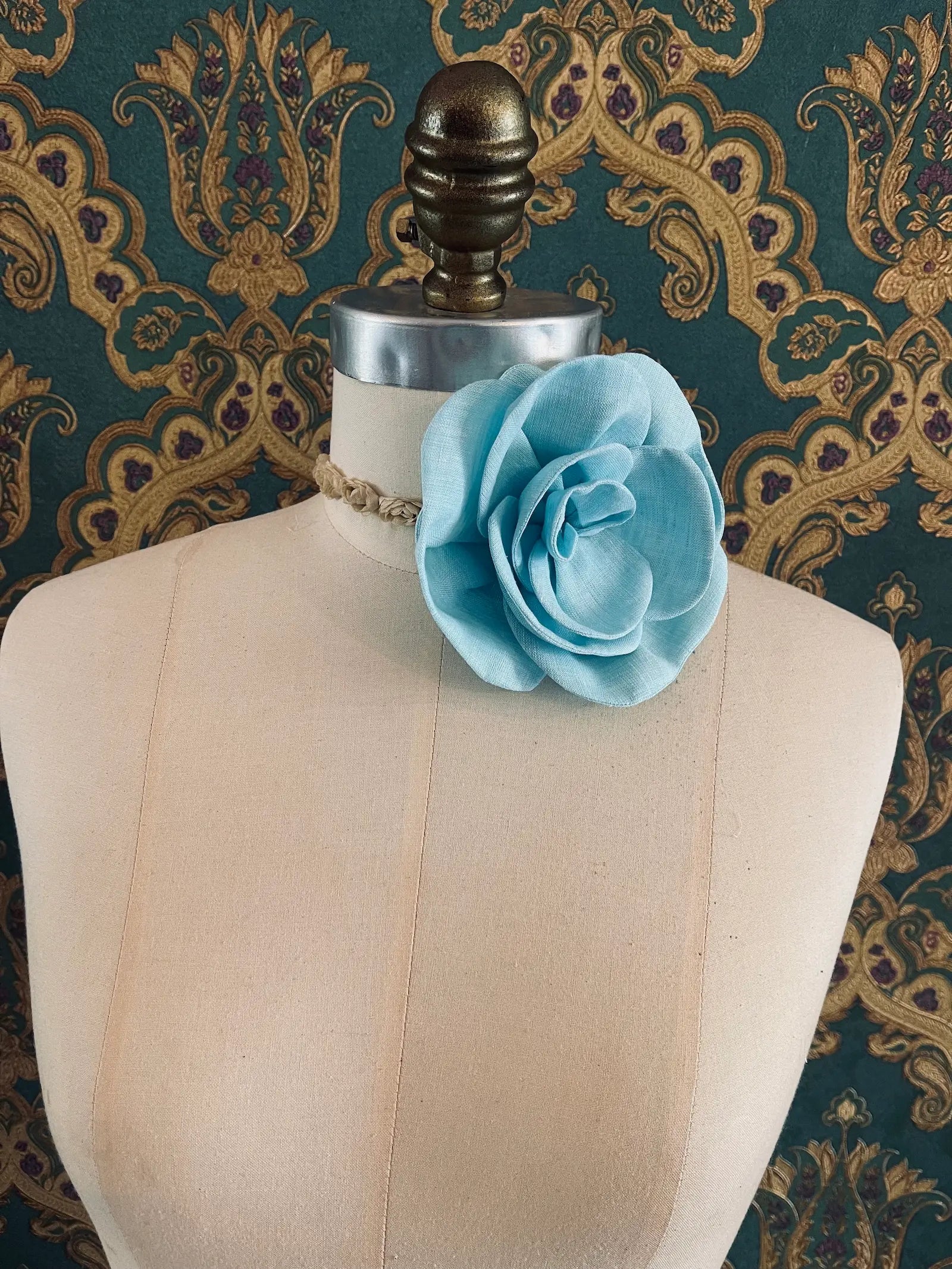 Broochella Florella small blue handmade linen flower brooch and choker  Pictured on a mannequin. The background is green and gold damask wallpaper.
