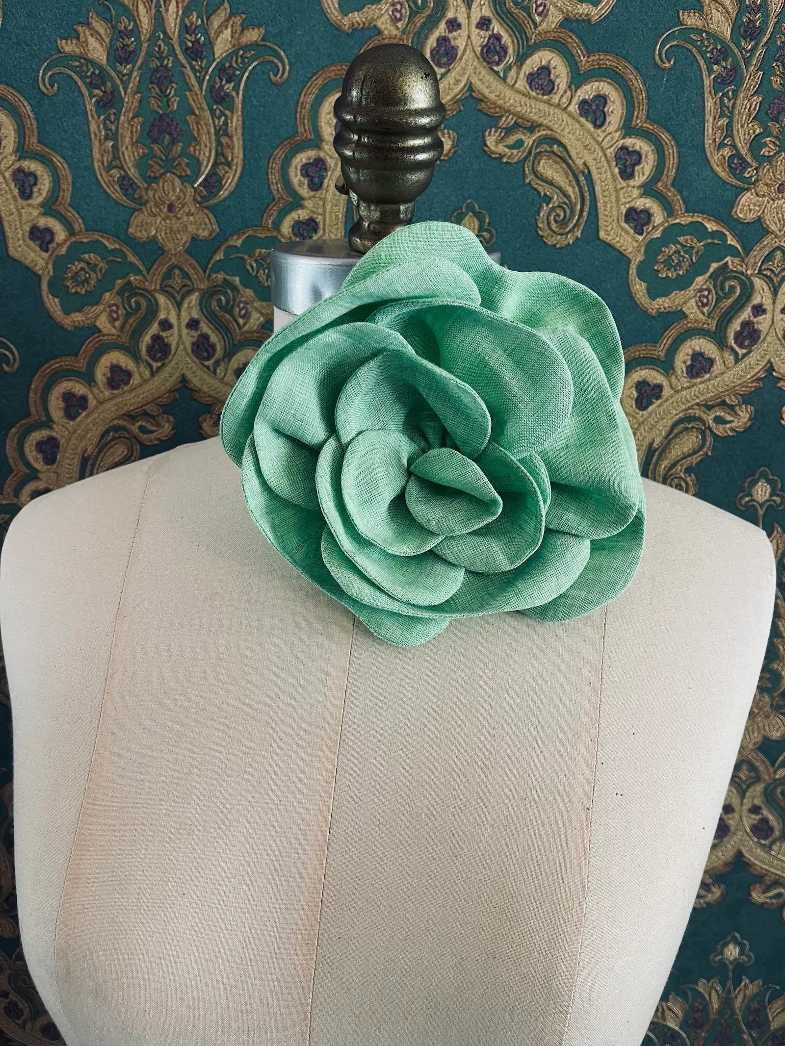 Broochella Florella large green handmade linen flower brooch and choker  Pictured on a mannequin. The background is green and gold damask wallpaper.