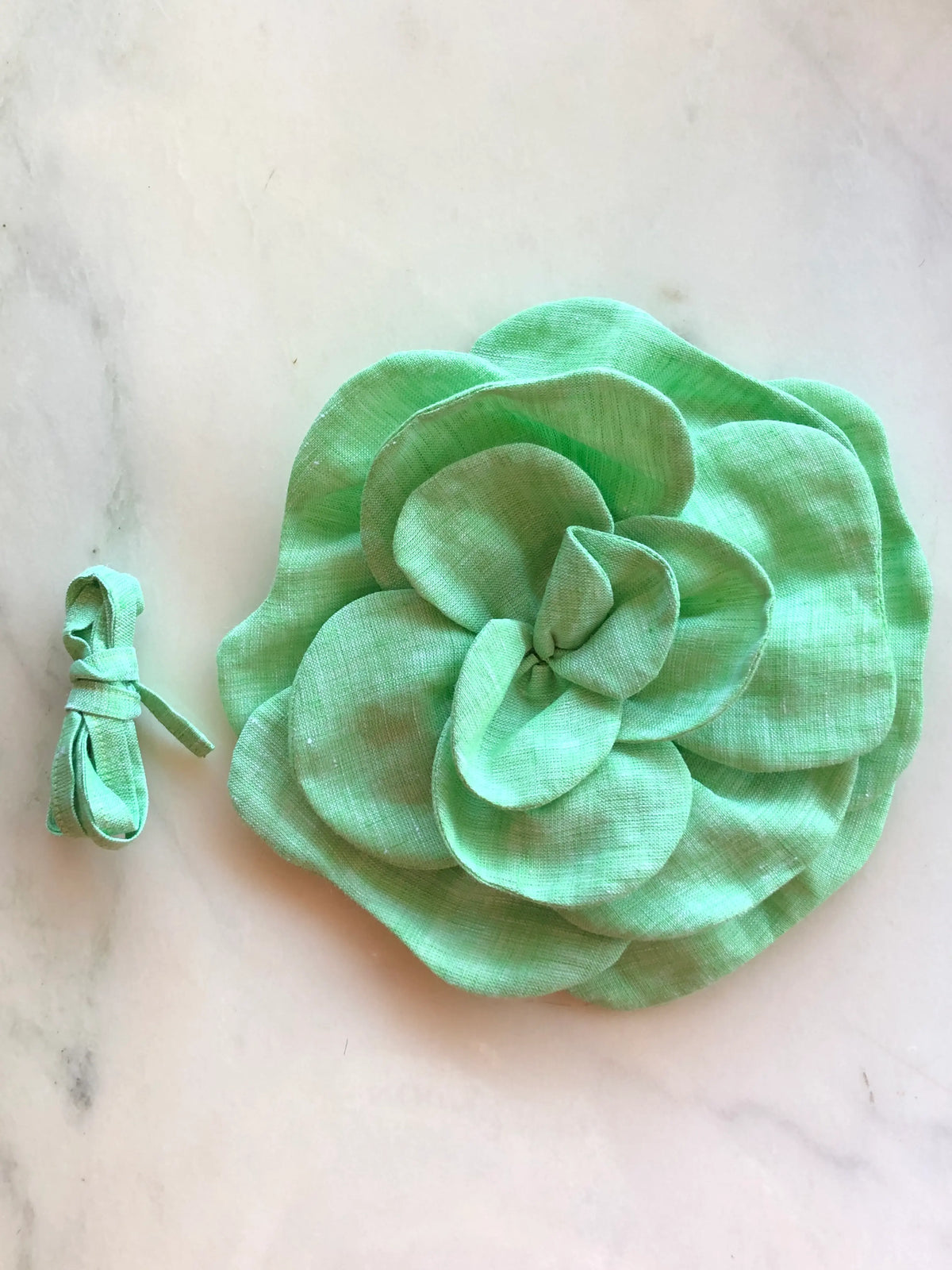 Broochella Florella Large Flower Choker in fresh green, featuring a sculptural layered flower with matching fabric ribbon, photographed on a white marble background with soft grey veining.