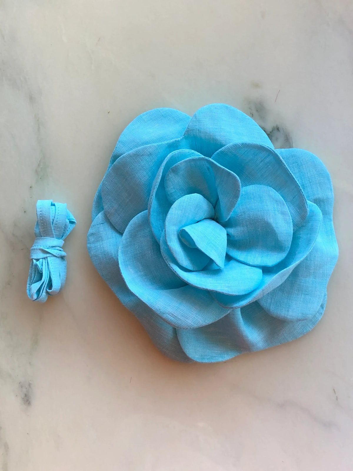 Broochella Florella Large Flower Choker in bright blue, featuring a sculptural layered flower with matching fabric ribbon, photographed on a white marble background with soft grey veining.