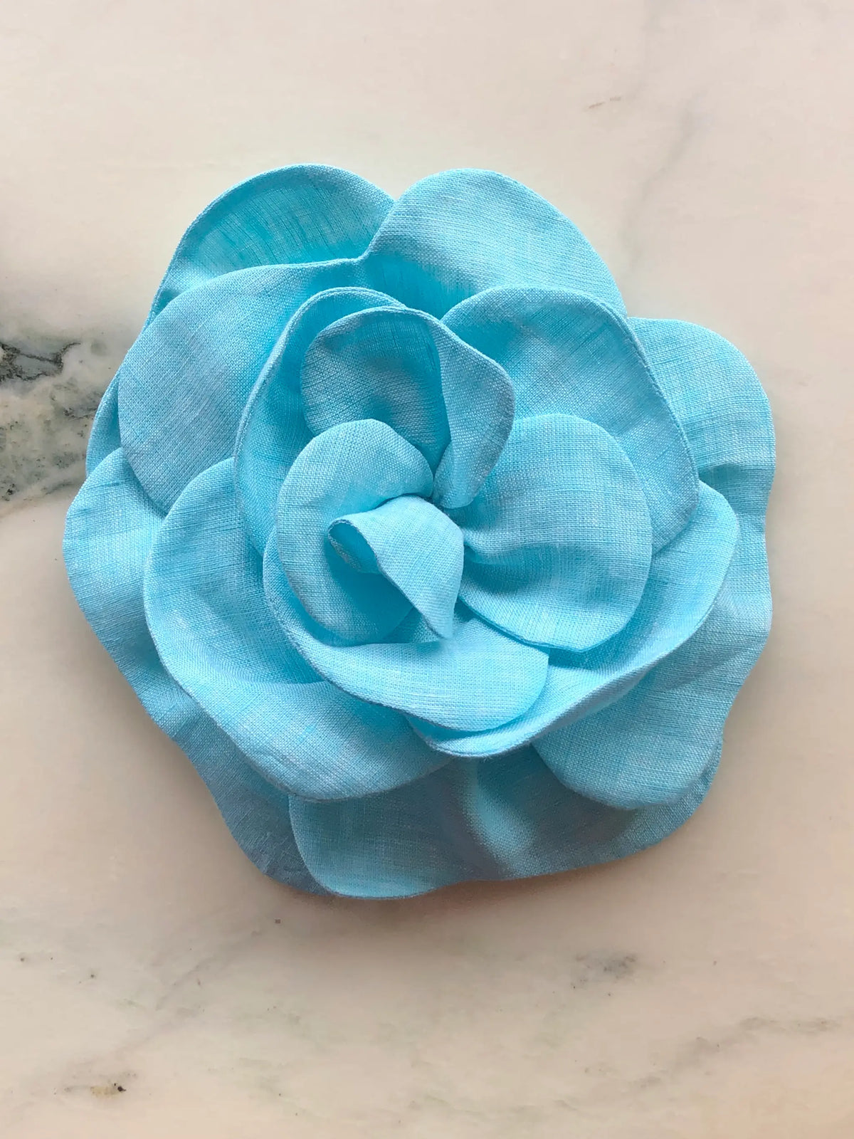 Large blue Broochella Florella Linen Flower Brooch with sculptural layered linen petals, photographed on a white marble background with soft grey veining.