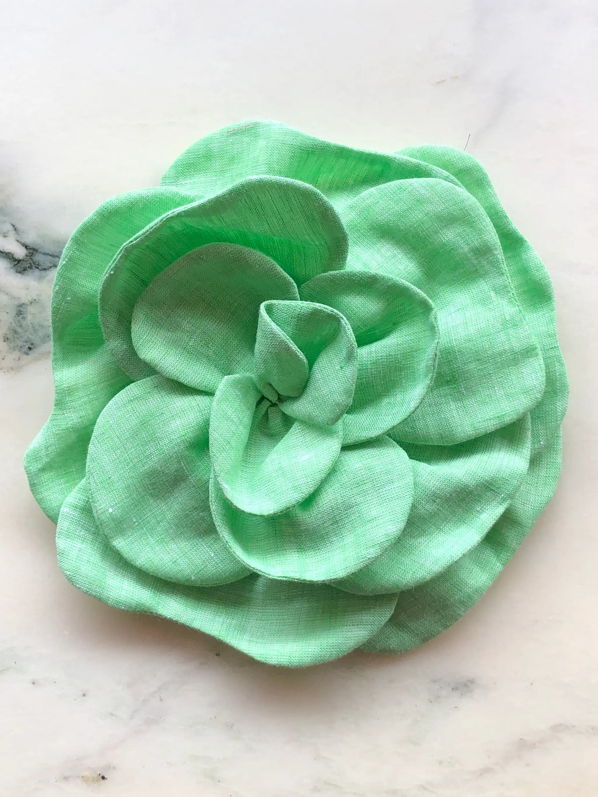 Large green Florella Linen Flower Brooch with sculptural layered linen petals, photographed on a white marble background with soft grey veining.