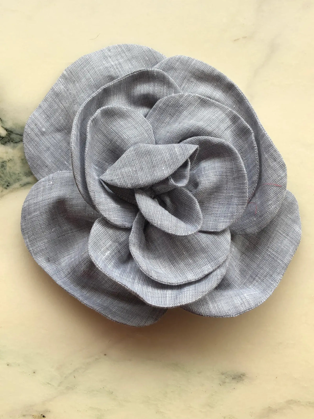 Large grey Broochella Florella Linen Flower Brooch with sculptural layered linen petals, photographed on a white marble background with soft grey veining.