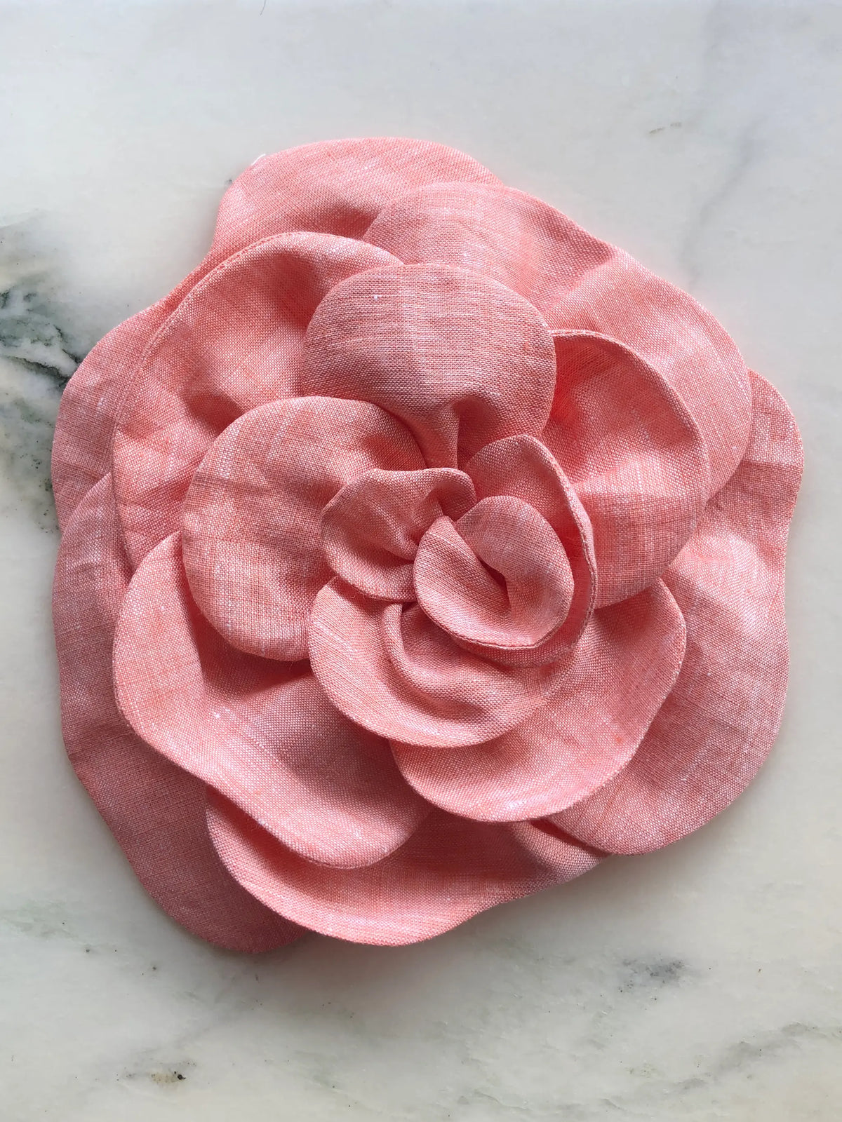 Large orange Broochella Florella Linen Flower Brooch with sculptural layered linen petals, photographed on a white marble background with soft grey veining.