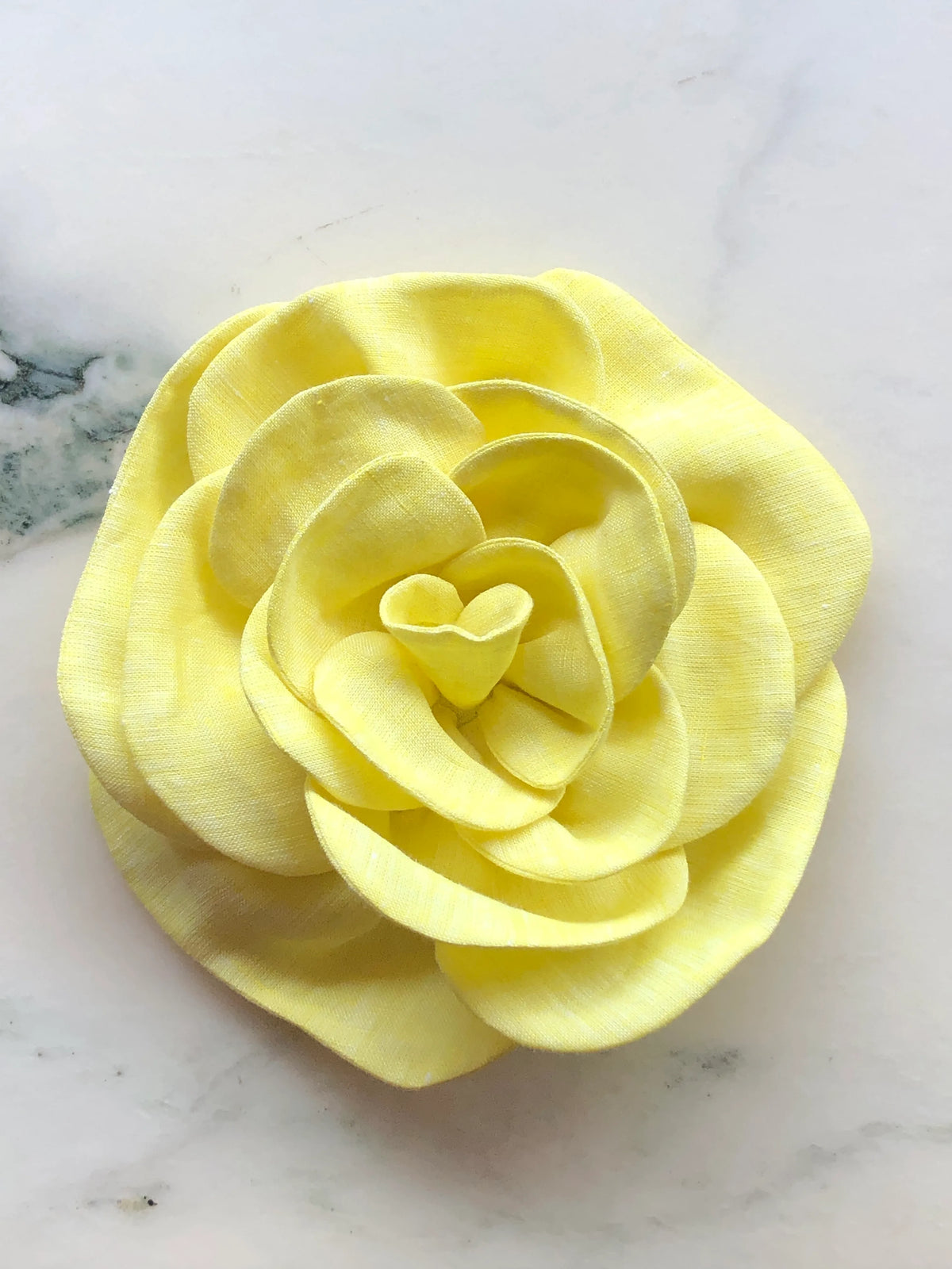 Large yellow Florella Linen Flower Brooch with sculptural layered petals, photographed on a white marble background with soft grey veining.