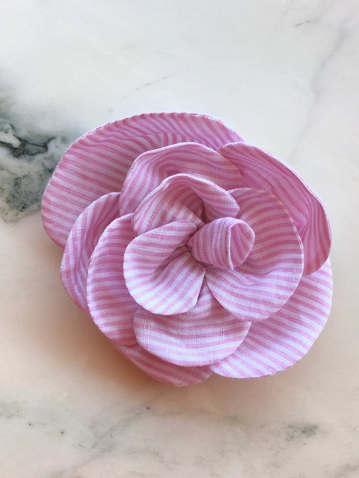 Florella pink and white striped linen flower brooch with sculptural layered petals, photographed on a white marble background with grey veining.