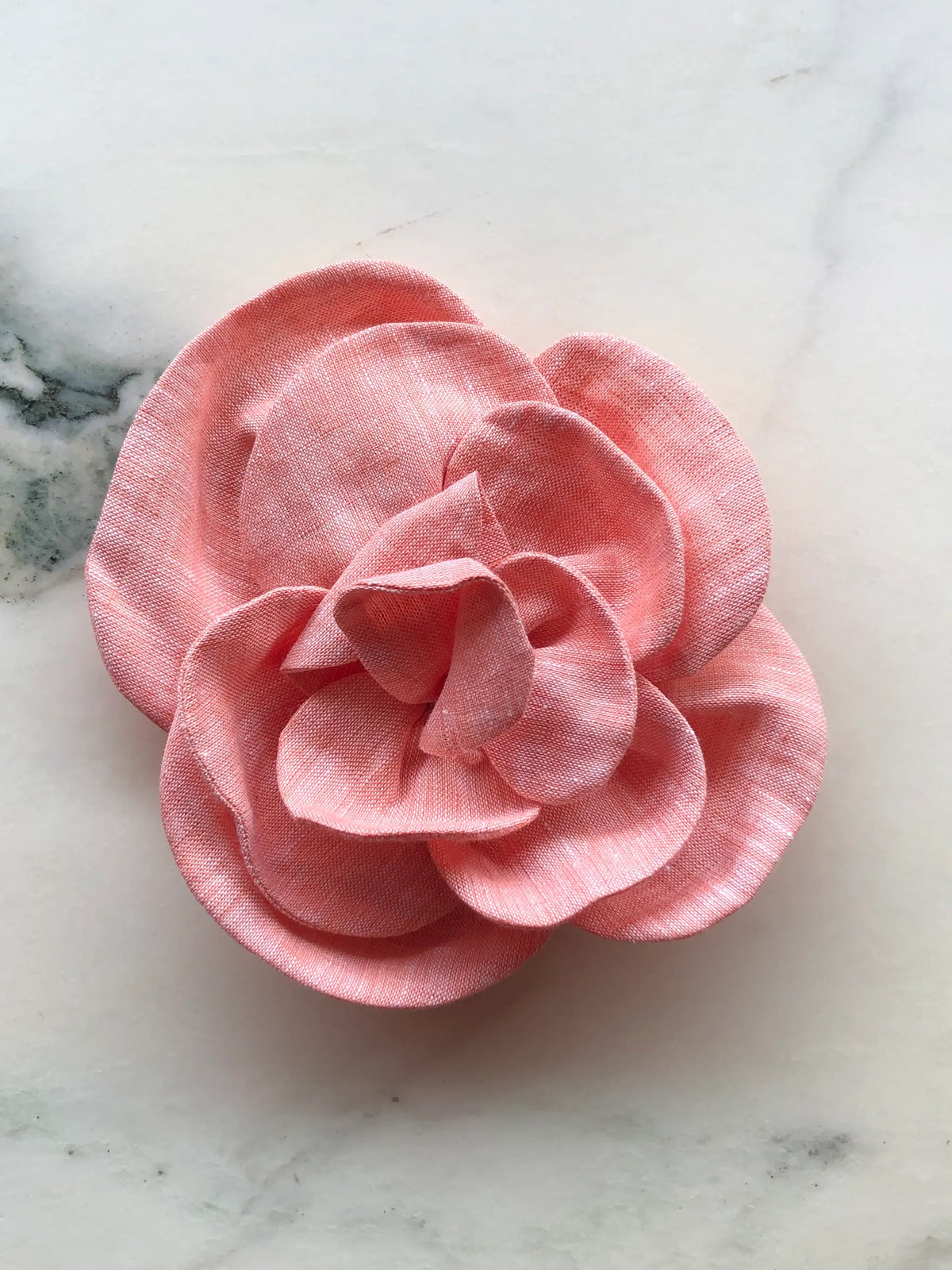 Small orange Broochella Florella Linen Flower Brooch with sculptural layered linen petals, photographed on a white marble background with soft grey veining.