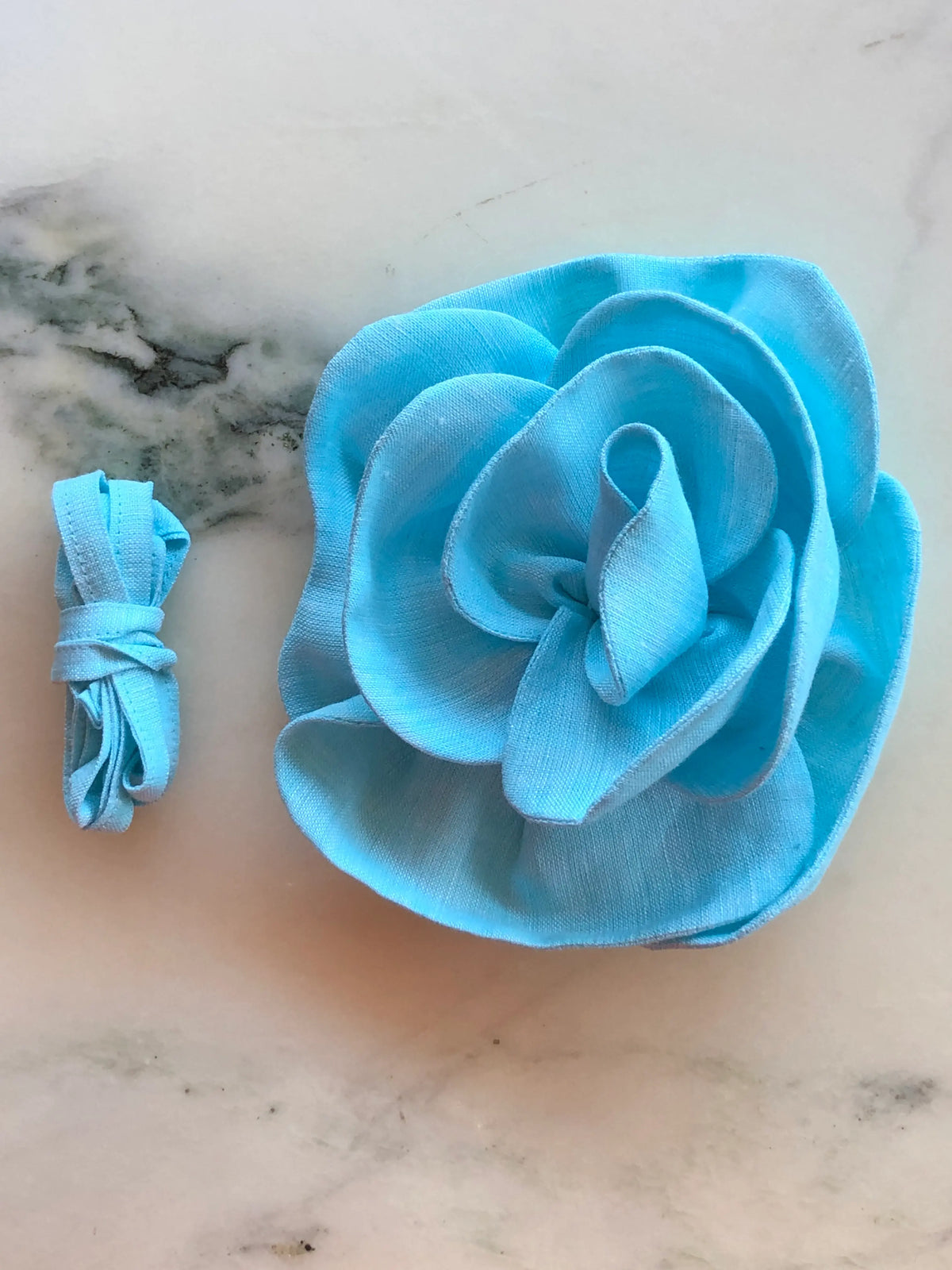 Broochella Florella small blue linen flower choker and brooch with matching ribbon, photographed on a white marble background.