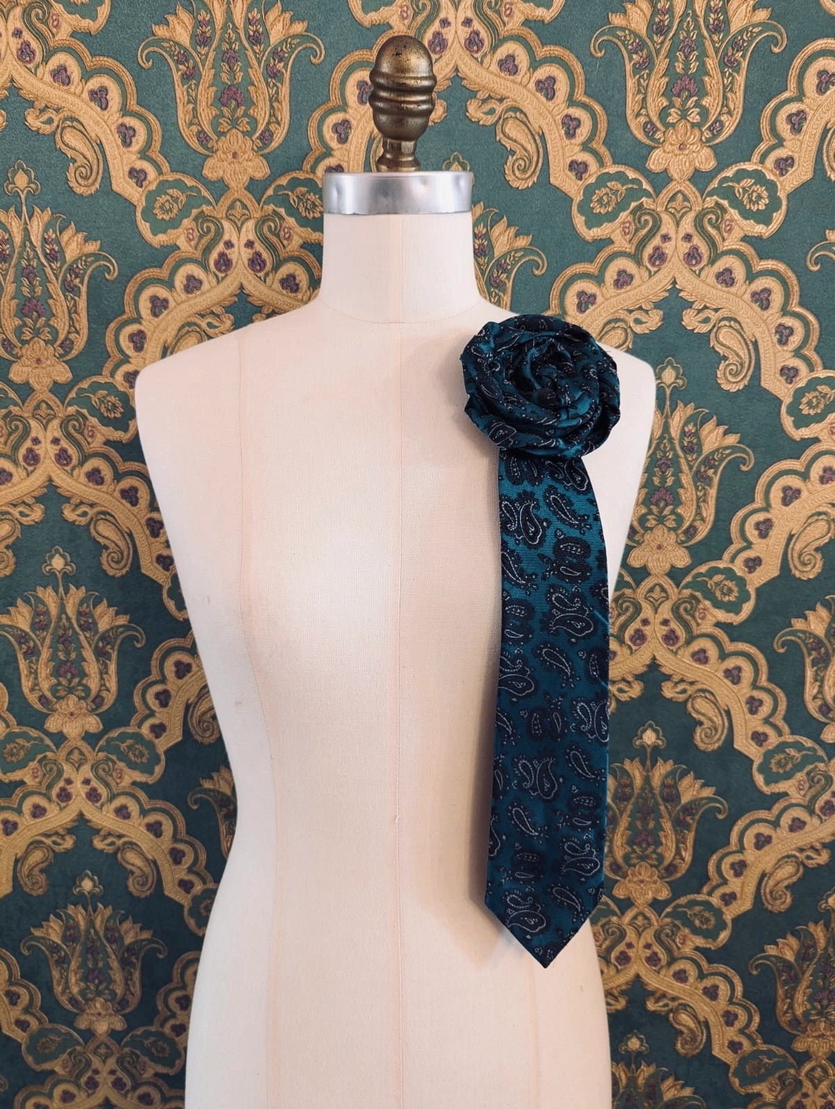 Broochella Fuente maurizio vintage up-cycled vintage handcrafted rosette tie in green and black paisley damask. Pinned on a mannequin. The background is green and gold damask wallpaper.
