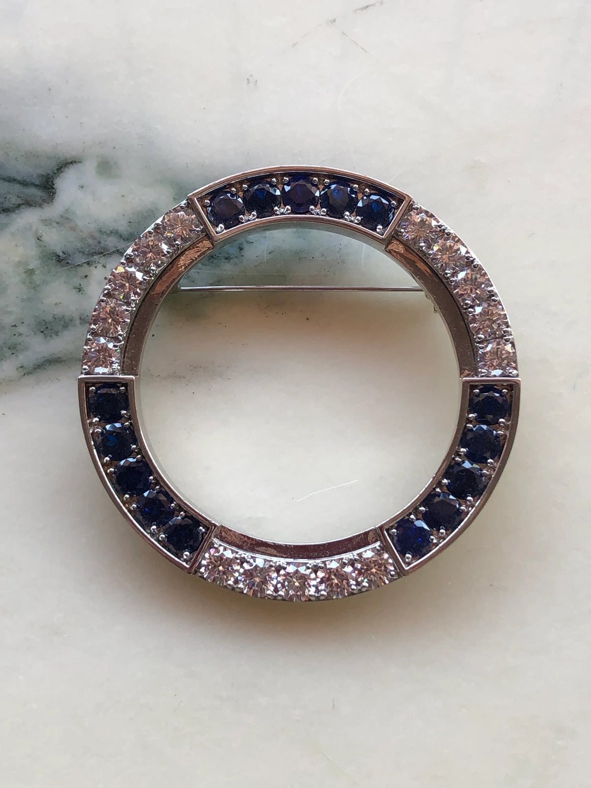 Broochella Full Moon Brooch Pin in silver-tone metal, featuring a circular open design set with alternating deep blue and clear crystal stones.