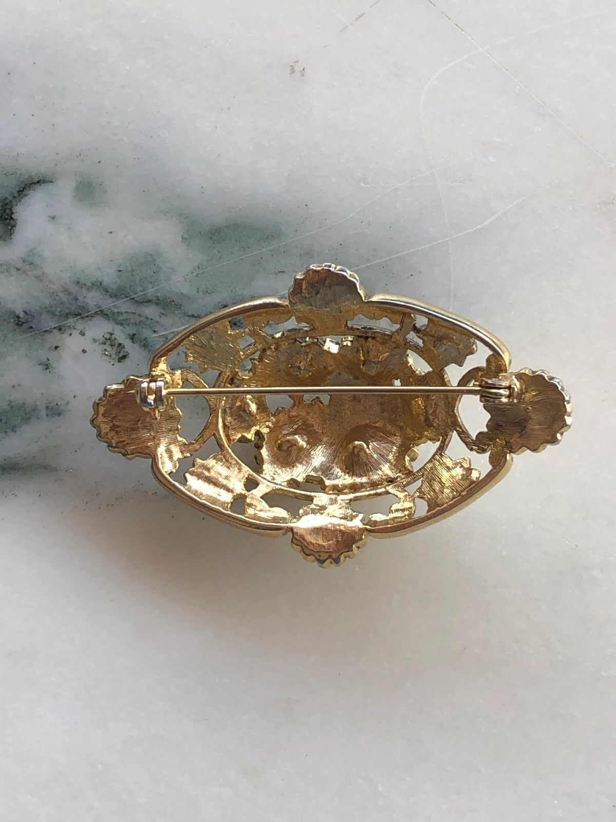 Broochella Giardino Fiorito Vintage Brooch Pin back view showing the gold-tone openwork floral construction and traditional pin fastening, photographed on white marble with grey-green veining.