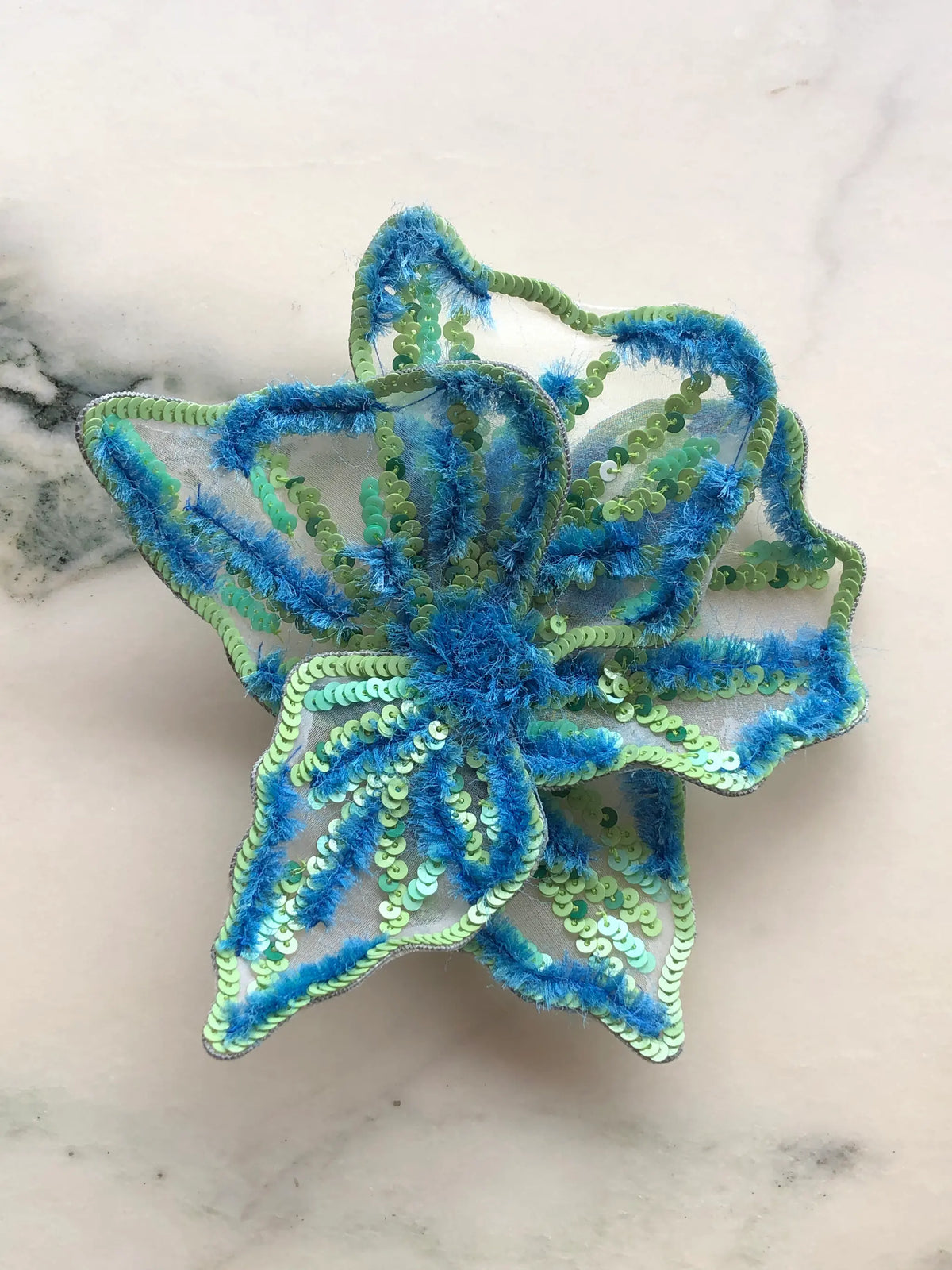 Broochella Men's Giglio di Tigre Small Flower Brooch Pin in blue, featuring sculptural translucent petals embellished with lime green and turquoise sequins, vibrant blue textured embroidery and a dimensional floral centre. A statement hand-embellished flower brooch for jackets, dresses and fashion-forward styling.