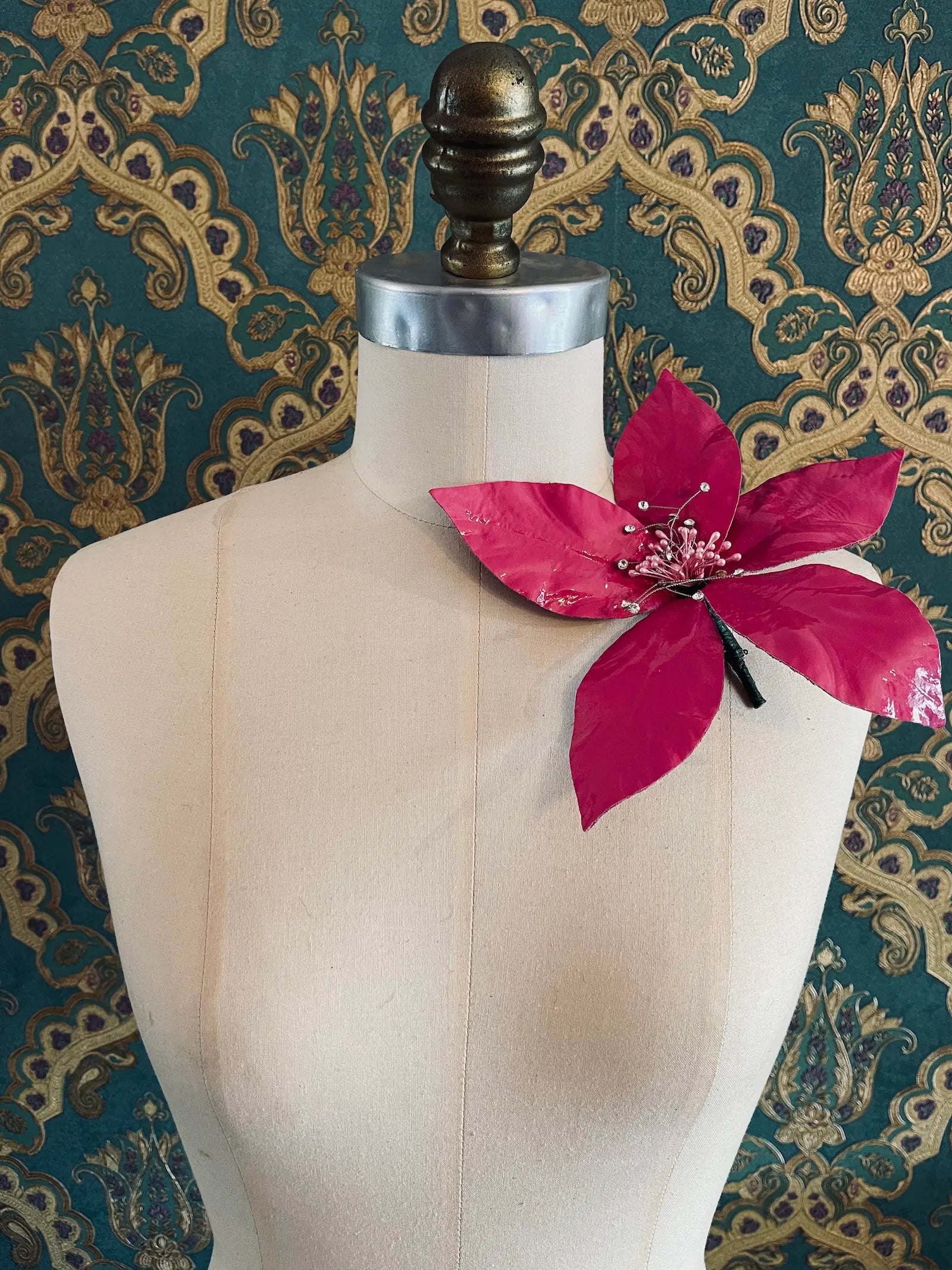 Broochella giglio handmade large patent leather flower in pink. Styled on a mannequin. The background is green and gold damask wallpaper