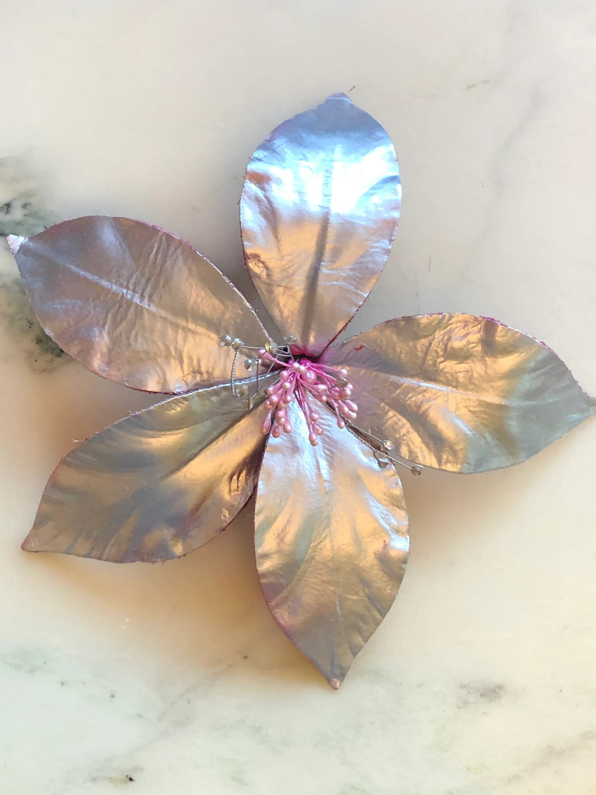 Broochella Giglio Flower Brooch Pin in glossy silver, featuring sculptural leather lily petals with a textured black centre and delicate crystal-tipped stamens on a cream marble background.