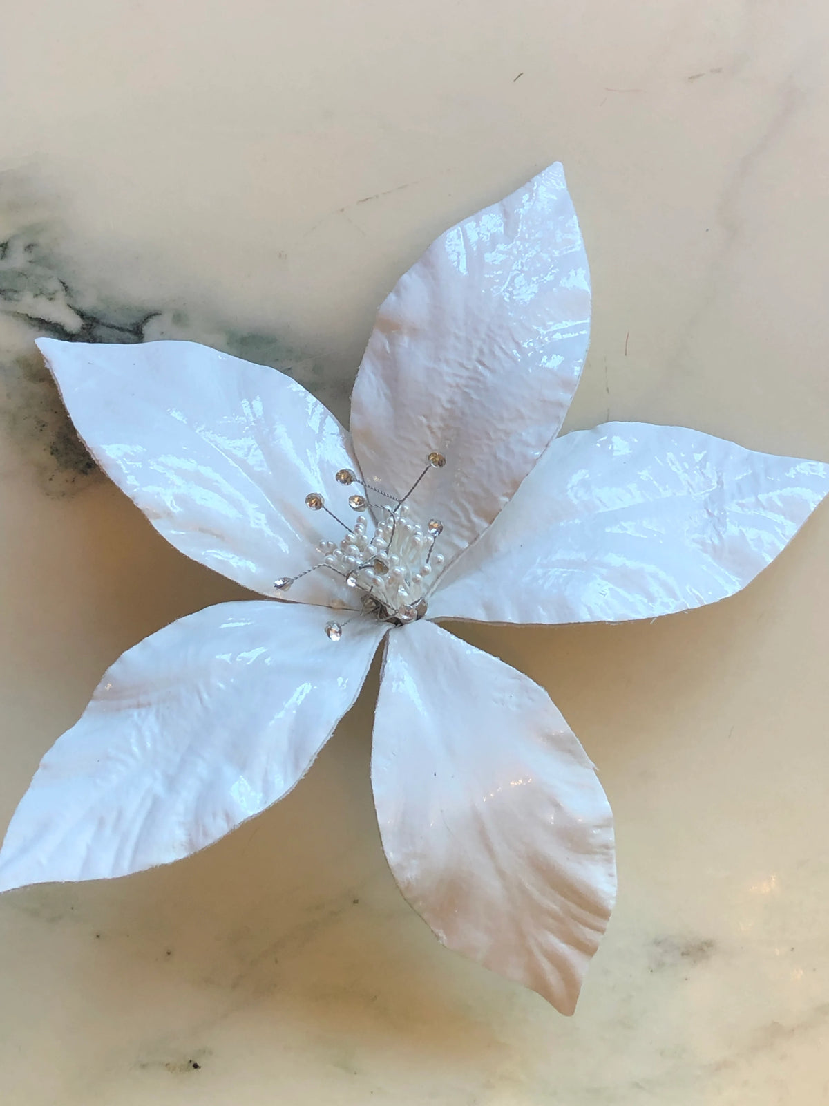 Broochella Giglio Flower Brooch Pin in glossy white featuring sculptural leather lily petals with a textured black centre and delicate crystal-tipped stamens on a cream marble background.