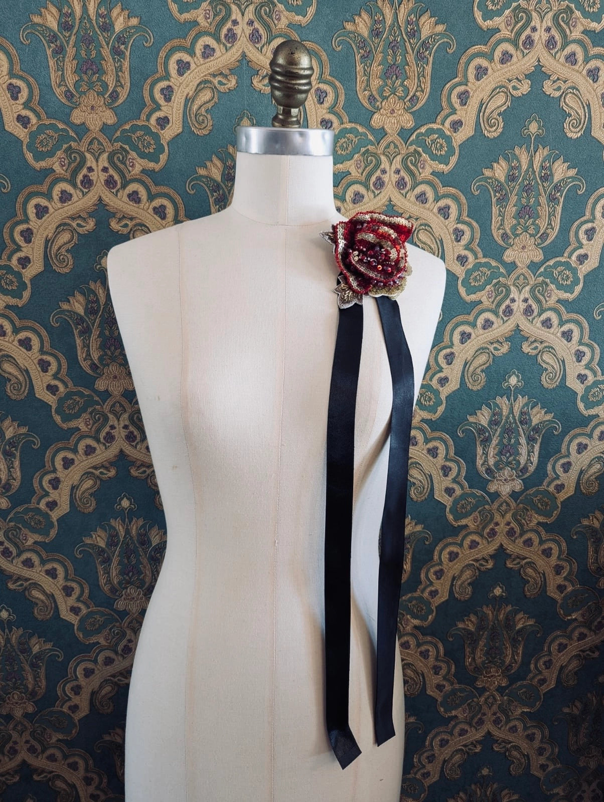 Broochella girocollo red and gold hand beaded and sequin flower chocker and brooch. Pictured on a mannequin. The background is green and gold damask wallpaper