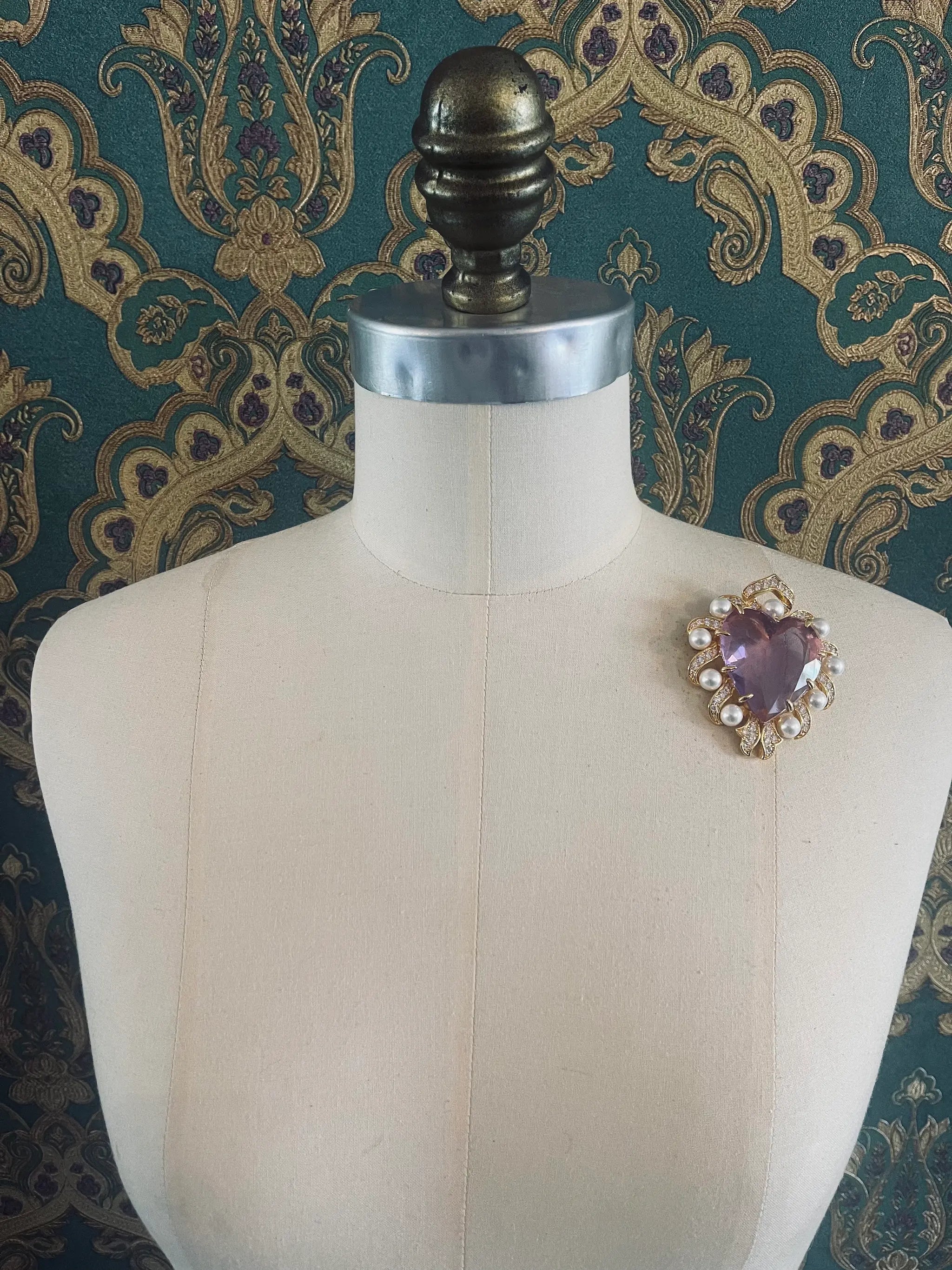 Broochella Giulietta e romeo gold and crystal brooch with pearls. Pictured on a mannequin. The background is green and gold damask wallpaper