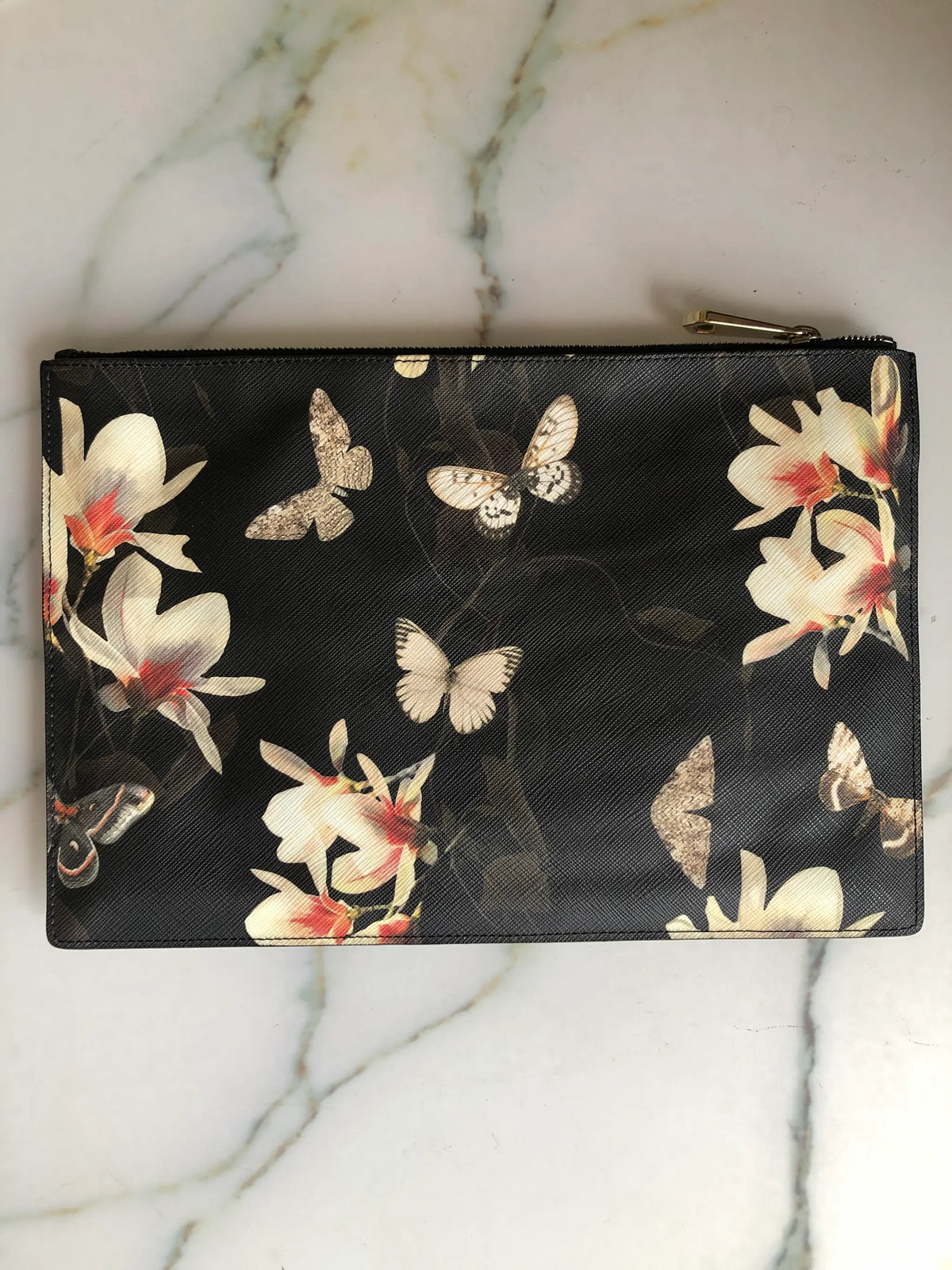 Genuine Givenchy black coated-canvas zip pouch featuring the Resort 2015 magnolia flower and butterfly print. Pictured on a white marble surface.
