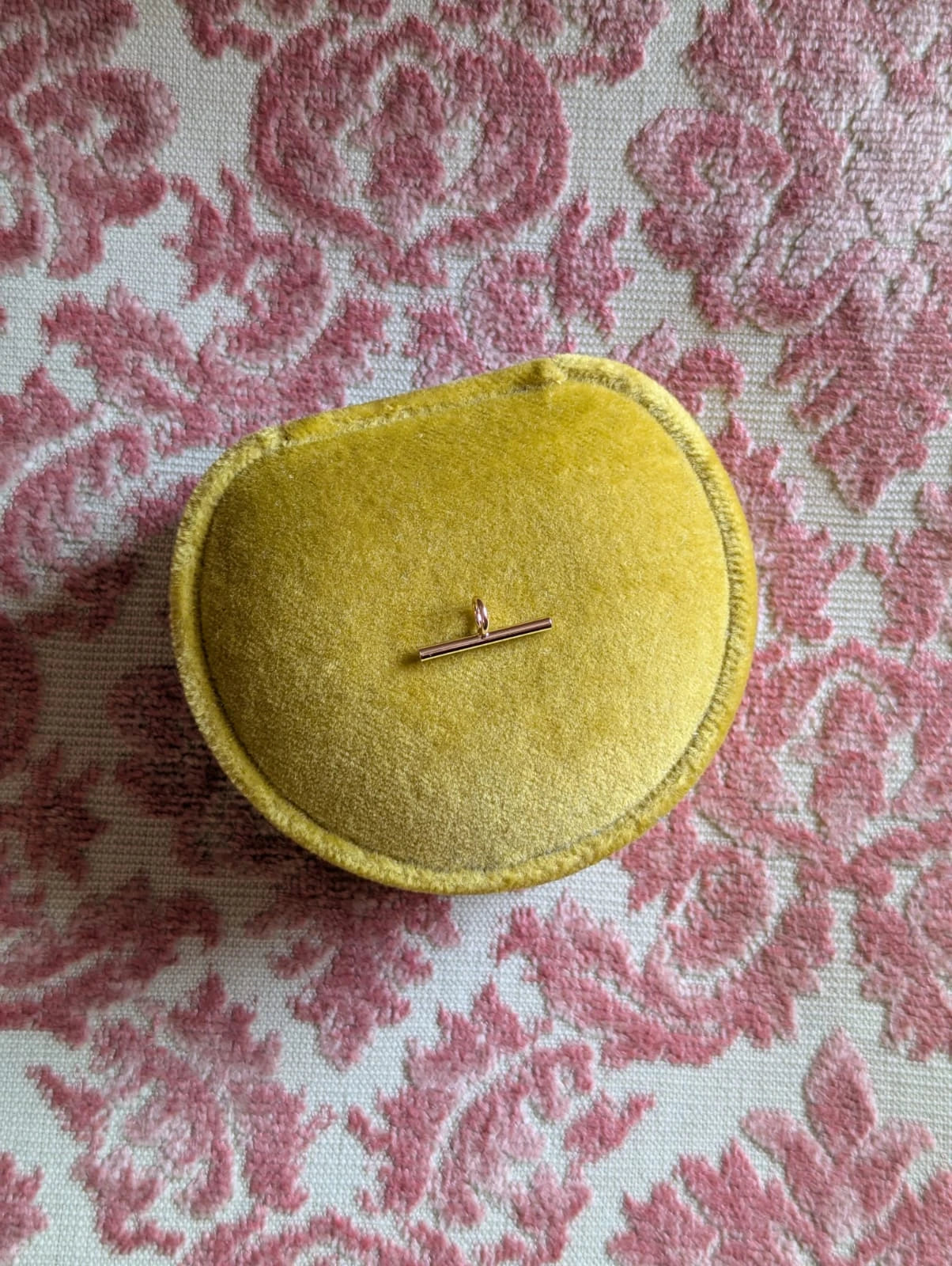 Broochella gold brooch to necklace brooch converter- extended bar. Pictured on a chartreuse ring box. The background is pale pink damask fabric.
