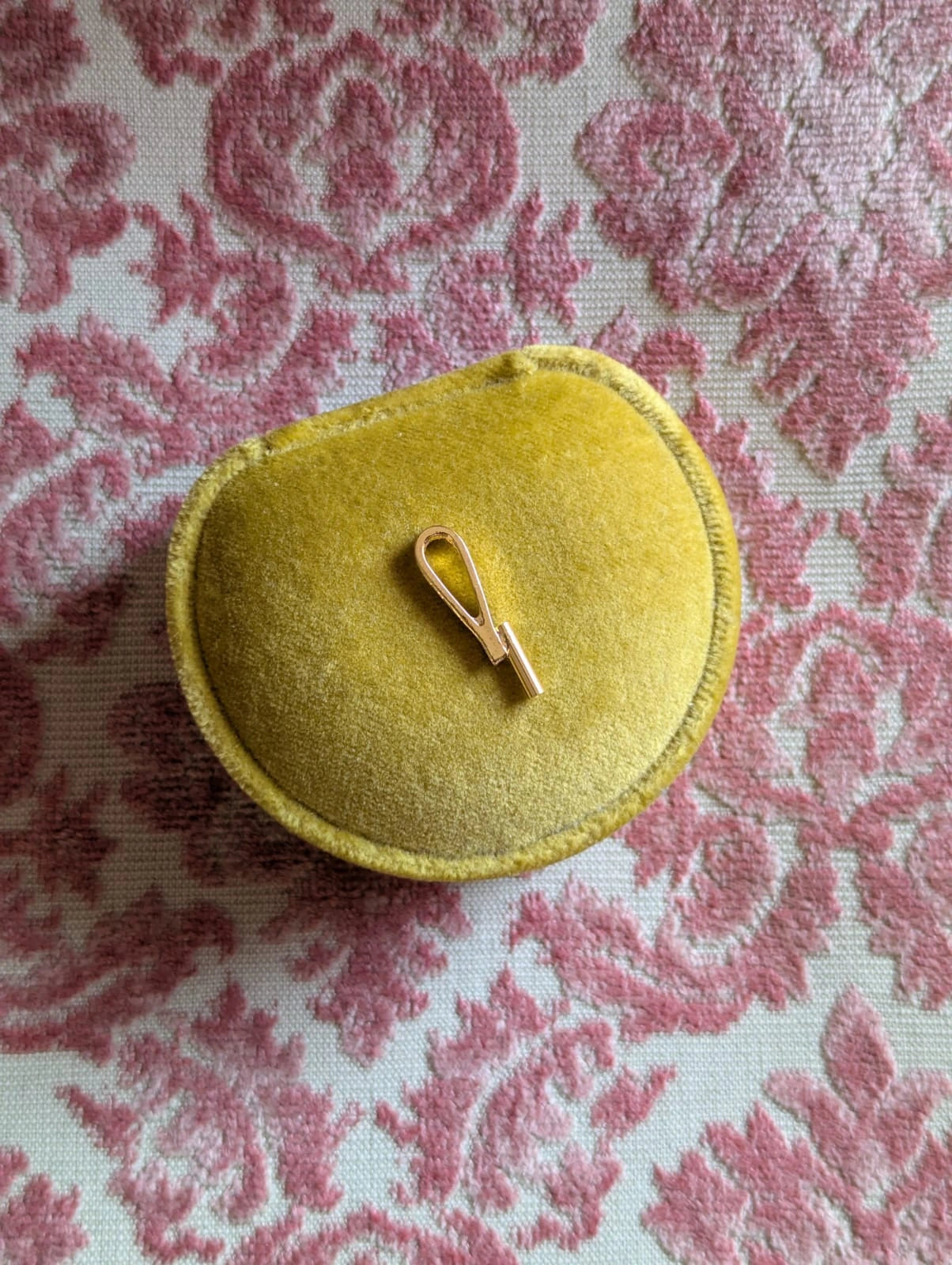 Broochella gold vertical brooch to necklace converter. Pictured on a chartreuse velvet ring box. The background is pink damask fabric.