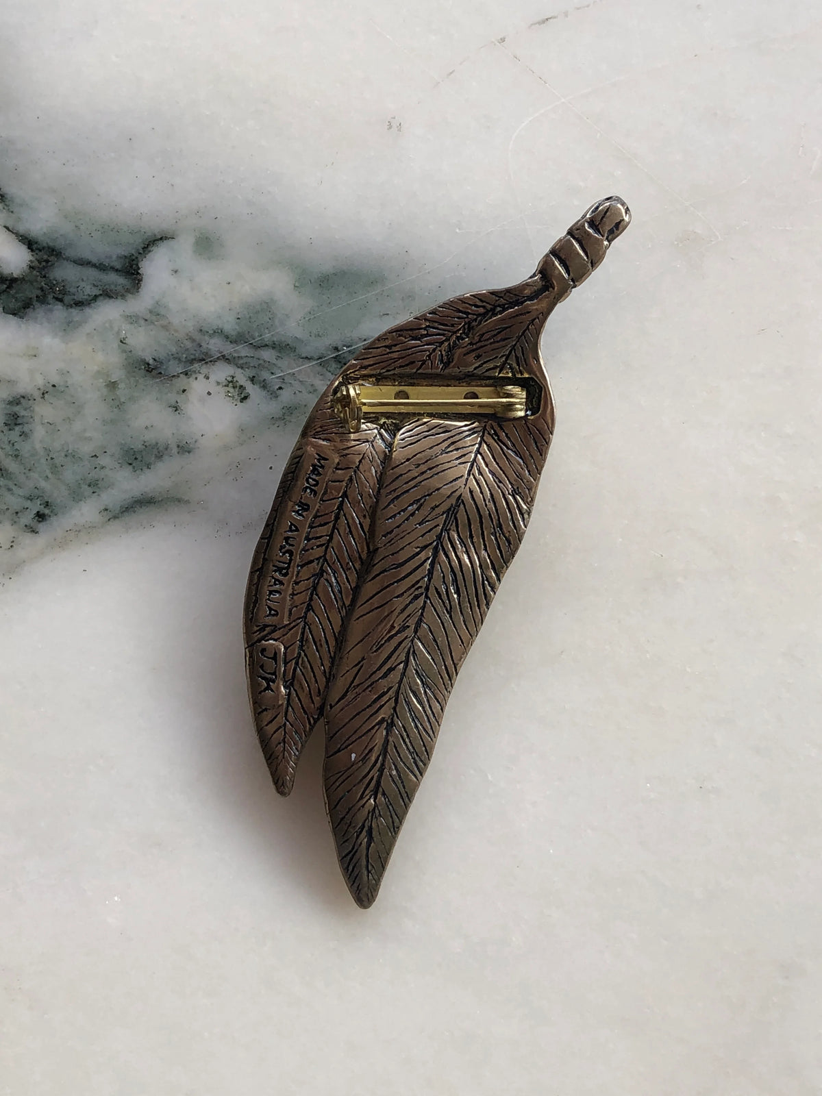 Broochella Golden Gumnut Trail Vintage Brooch back view showing textured eucalyptus leaves, Made in Australia marking and gold-tone pin fastening, photographed on white marble with natural grey-green veining.