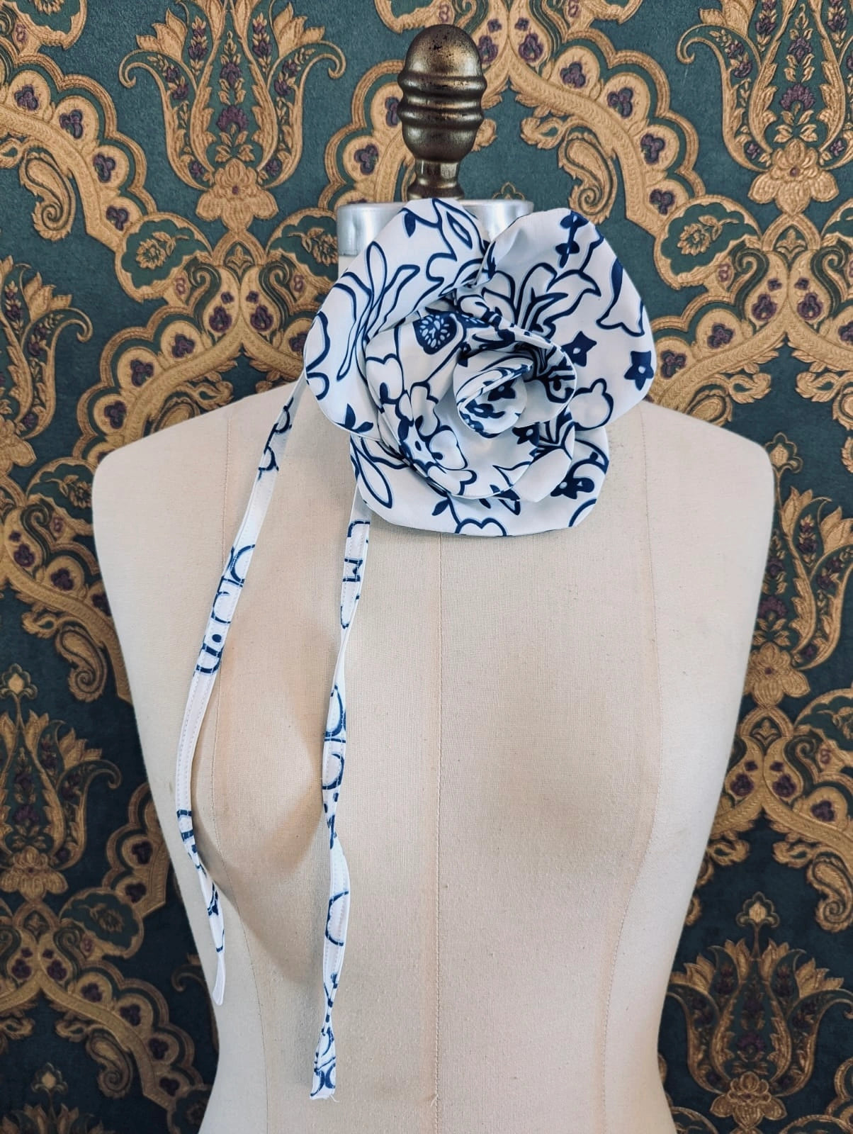 Broochella electra flower choker and brooch with blue and white floral print.  Pictured on a mannequin.  The background is green and gold damask wallpaper.