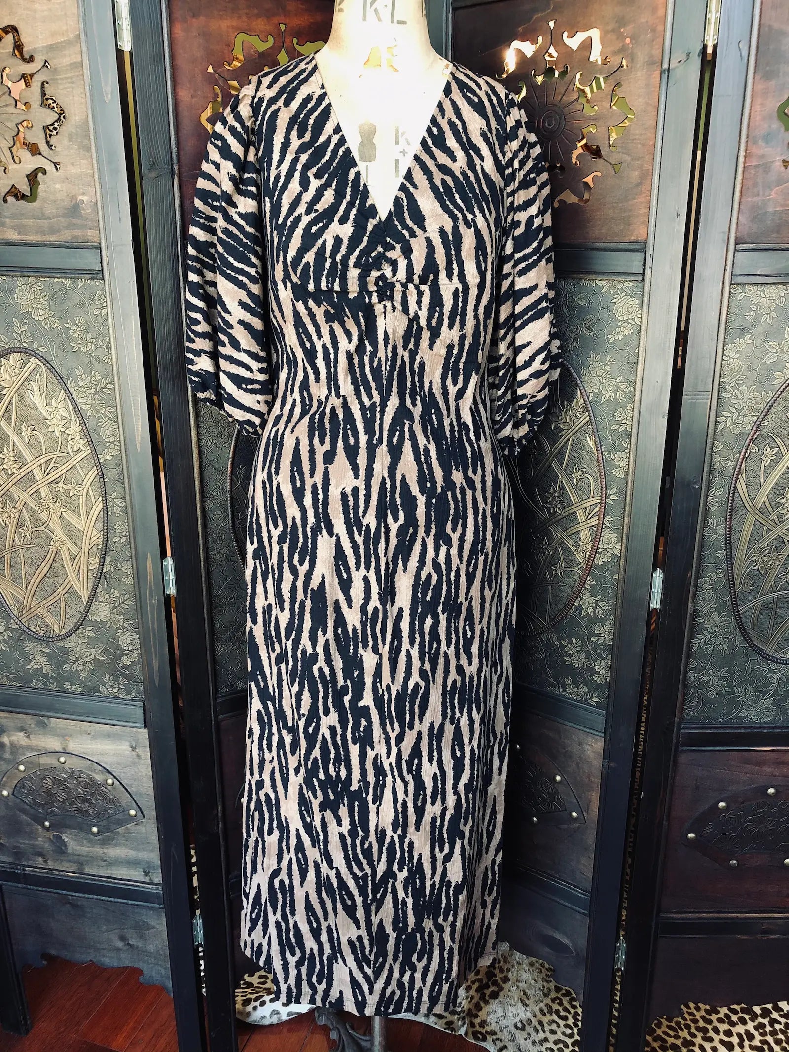 Broochella H&M, Small, 100% cotton
Black and beige zebra print dress with
V-neckline with gathered detail 3/4 sleeves. Midi length. It is pictured on a vintage mannequin. The background is an ornate, dark wood room divider. 