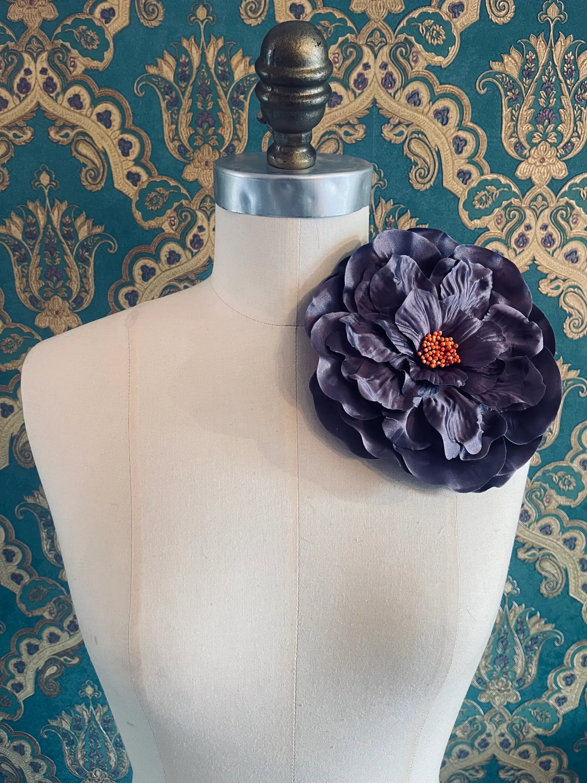 Broochella Ibisco large handmade purple flwer brooch. Styled on a mannequin. The background is green and gold damask wallpaper