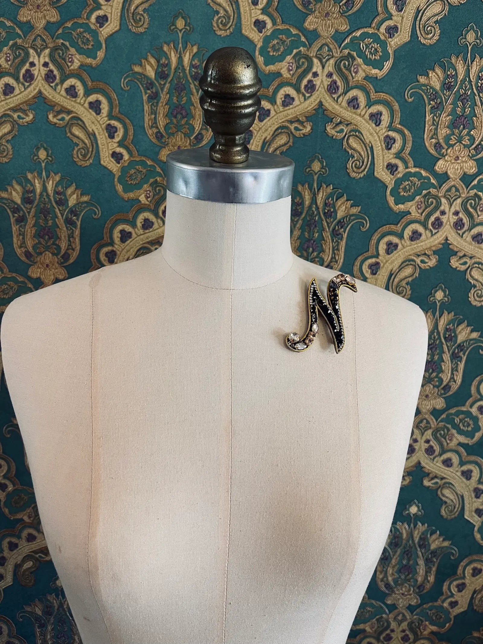 Broochella letter N hand beaded initial alphabet brooch in gold and black beads and sequins. Pictured on a mannequin. The background is green and gold damask wallpaper.