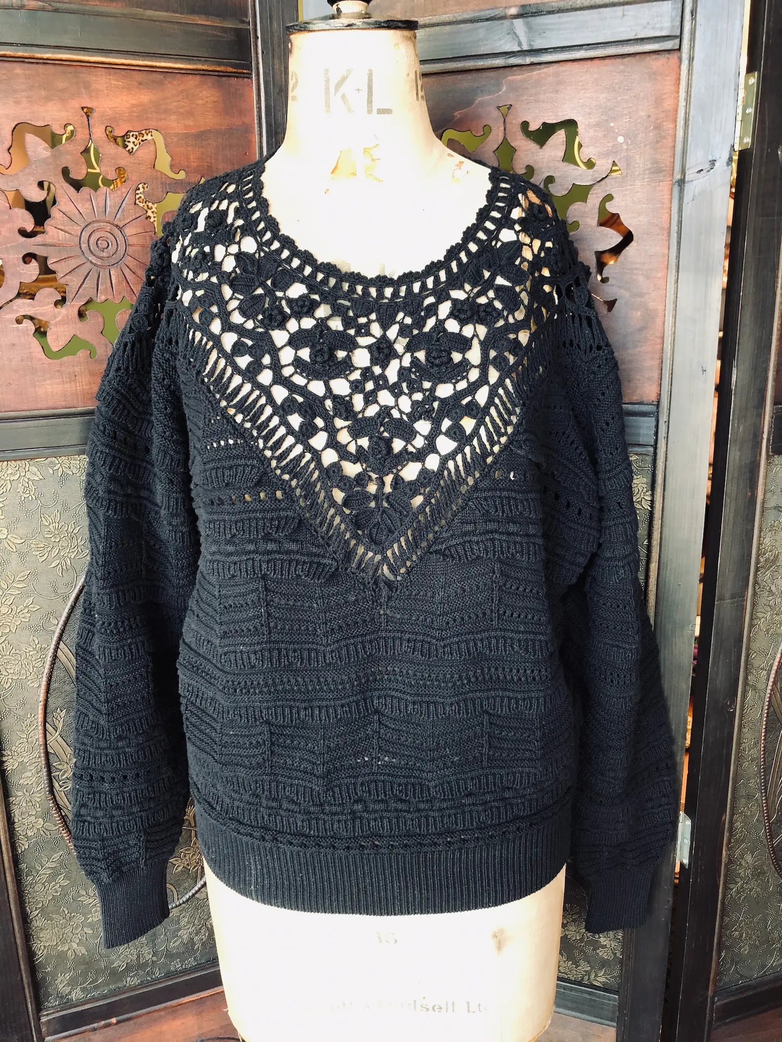 Broochella Isabel Marant, size Large knit sweater.  100% Cotton, black, intricate crochet lace neckline, long sleeves and ribbed hem and cuffs. It is pictured on a vintage mannequin. The background is an ornate, dark wood, vintage room divider. 
