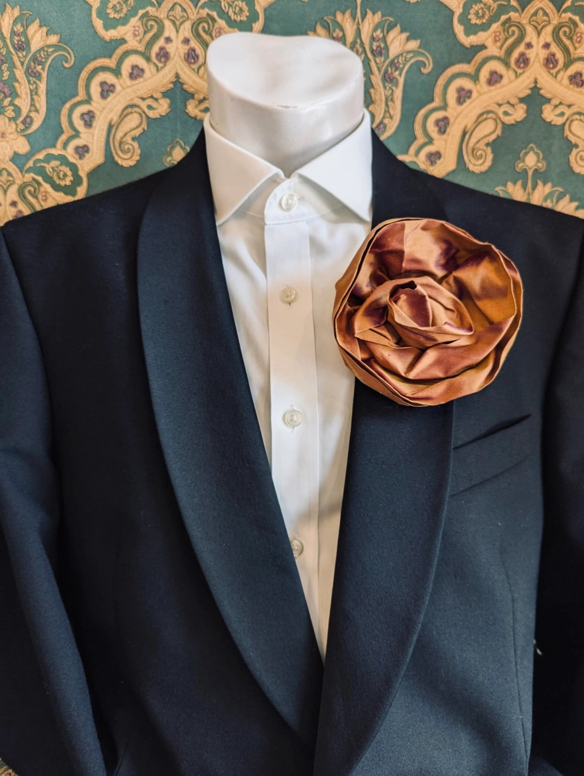 Broochella Isabella Rossellini handmade silk rosette flower brooch in rust. Pictured on a mannequin.  The background is green and gold damask wallpaper