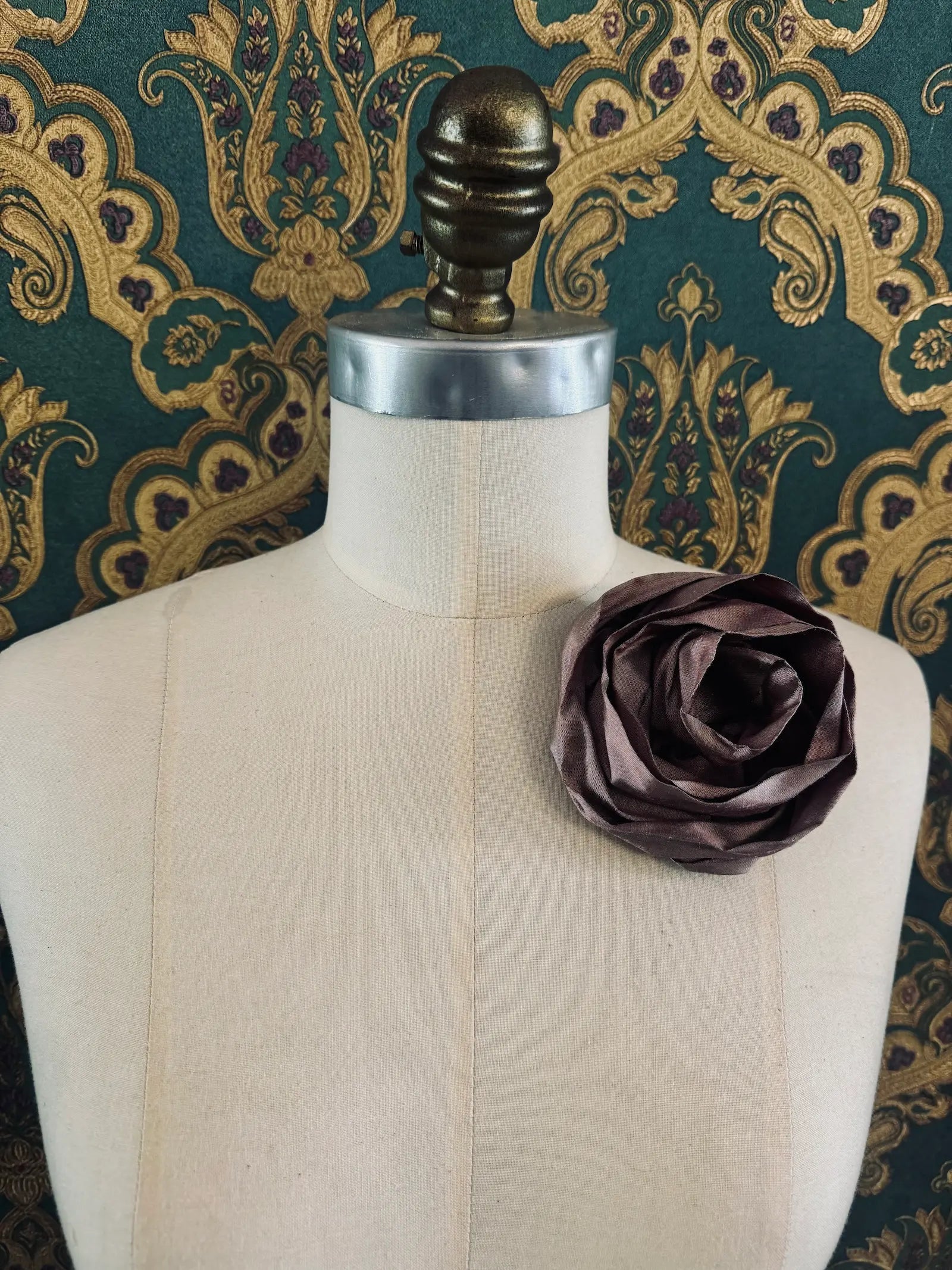Broochella Isabella Rossellini handmade silk rosette flower brooch in purple. Pictured on a mannequin.  The background is green and gold damask wallpaper