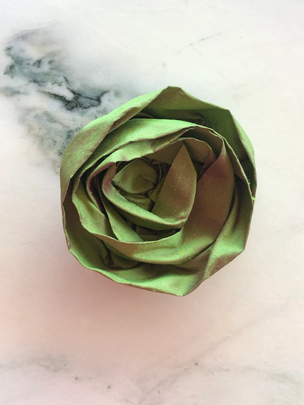 Handmade Broochella Isabella Rossellini designer silk rosette brooch for men in green, featuring layered fabric petals for distinctive suit and blazer styling, photographed on white marble.