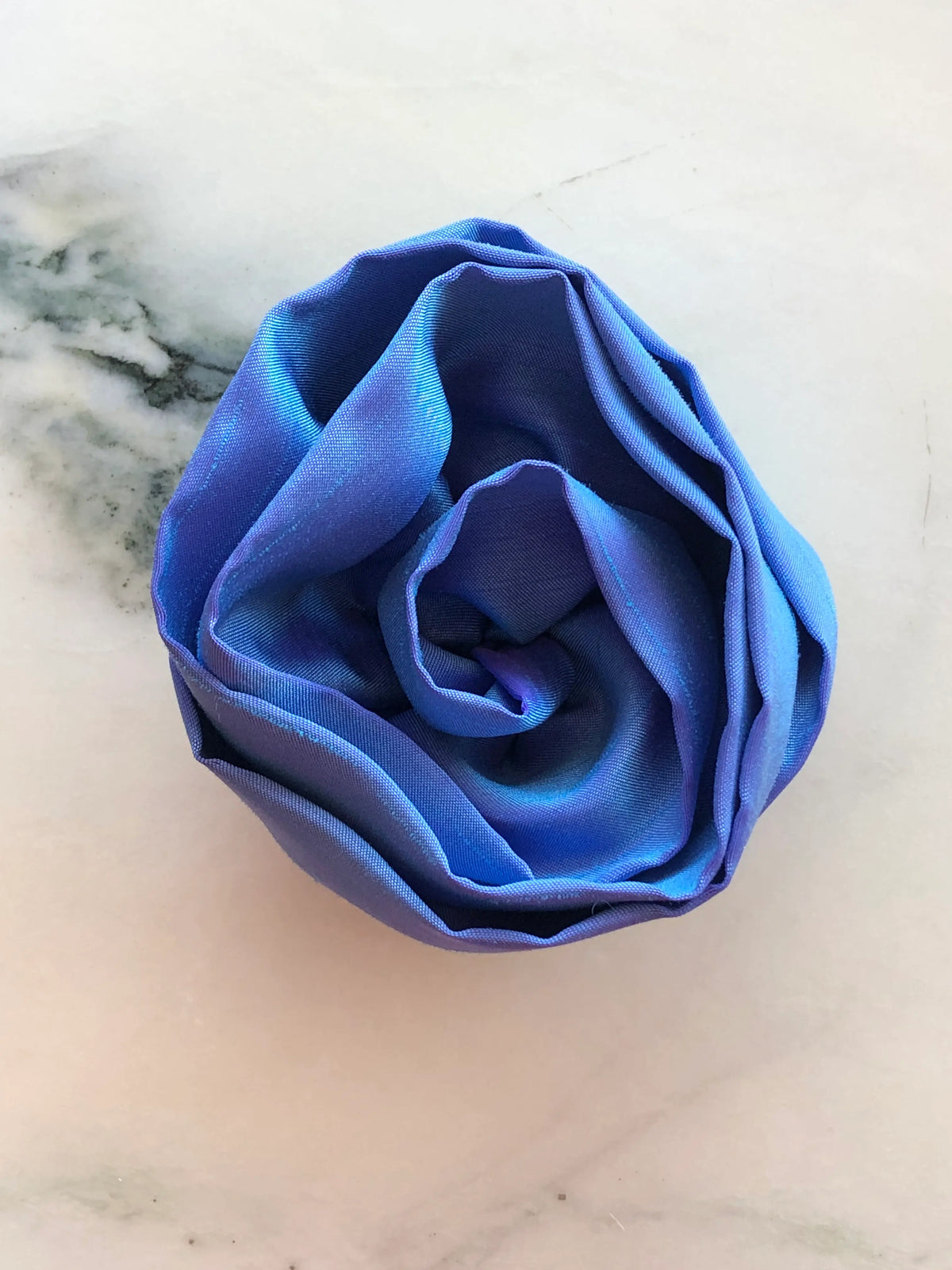 Handmade Broochella Isabella Rossellini designer silk rosette brooch in powder blue, with sculptural overlapping rose petals creating a statement flower accessory, photographed on white marble.