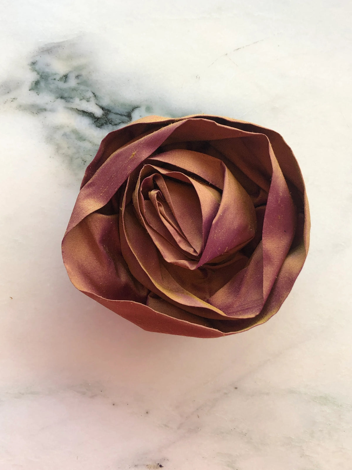 Handmade Broochella Isabella Rossellini designer silk rosette brooch for men in warm rust, a sculptural flower lapel accessory for jackets and suits, photographed on white marble.