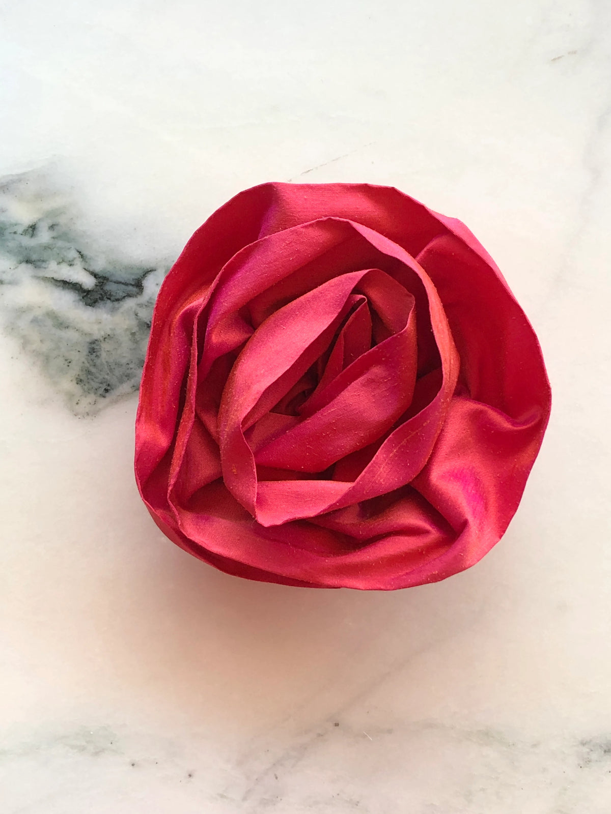 Handmade Broochella Isabella Rossellini designer silk rosette brooch in rich tangerine, featuring sculptural layered rose petals, photographed on white marble.
