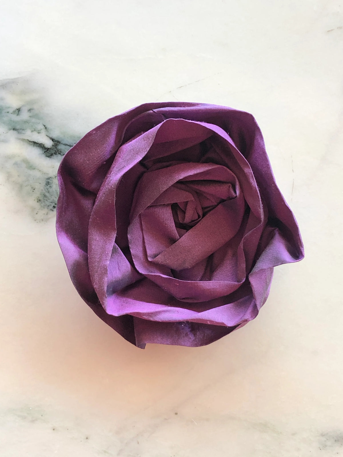 Handmade Broochella Isabella Rossellini designer silk rosette brooch for men in rich violet, featuring sculptural layered petals for statement menswear styling, photographed on white marble.