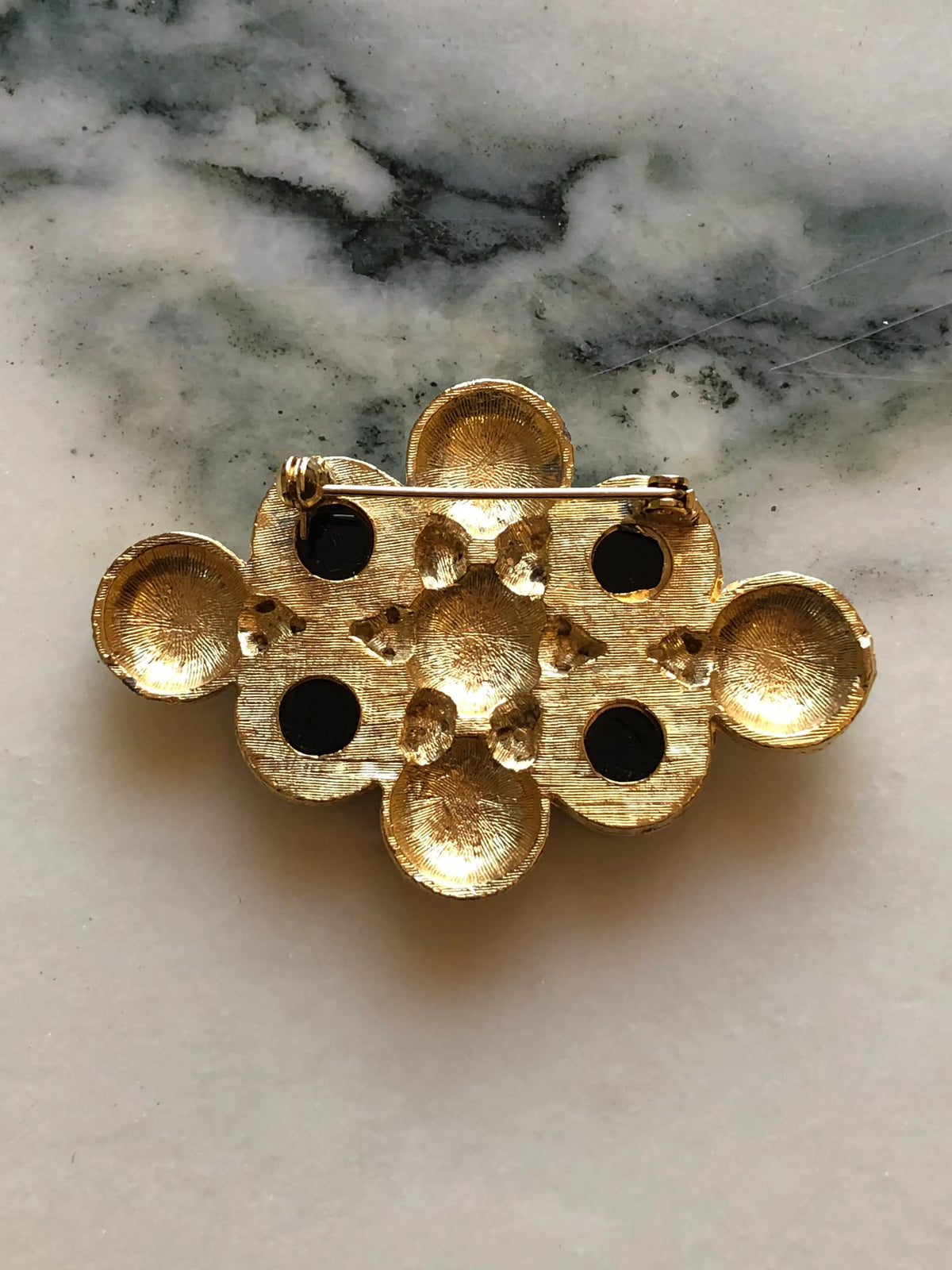 The back view of Broochella Isabella Vintage Black & Gold Statement Brooch featuring four faceted black stones, faux pearls and textured gold-tone spiral motifs on a cream and grey marble background.