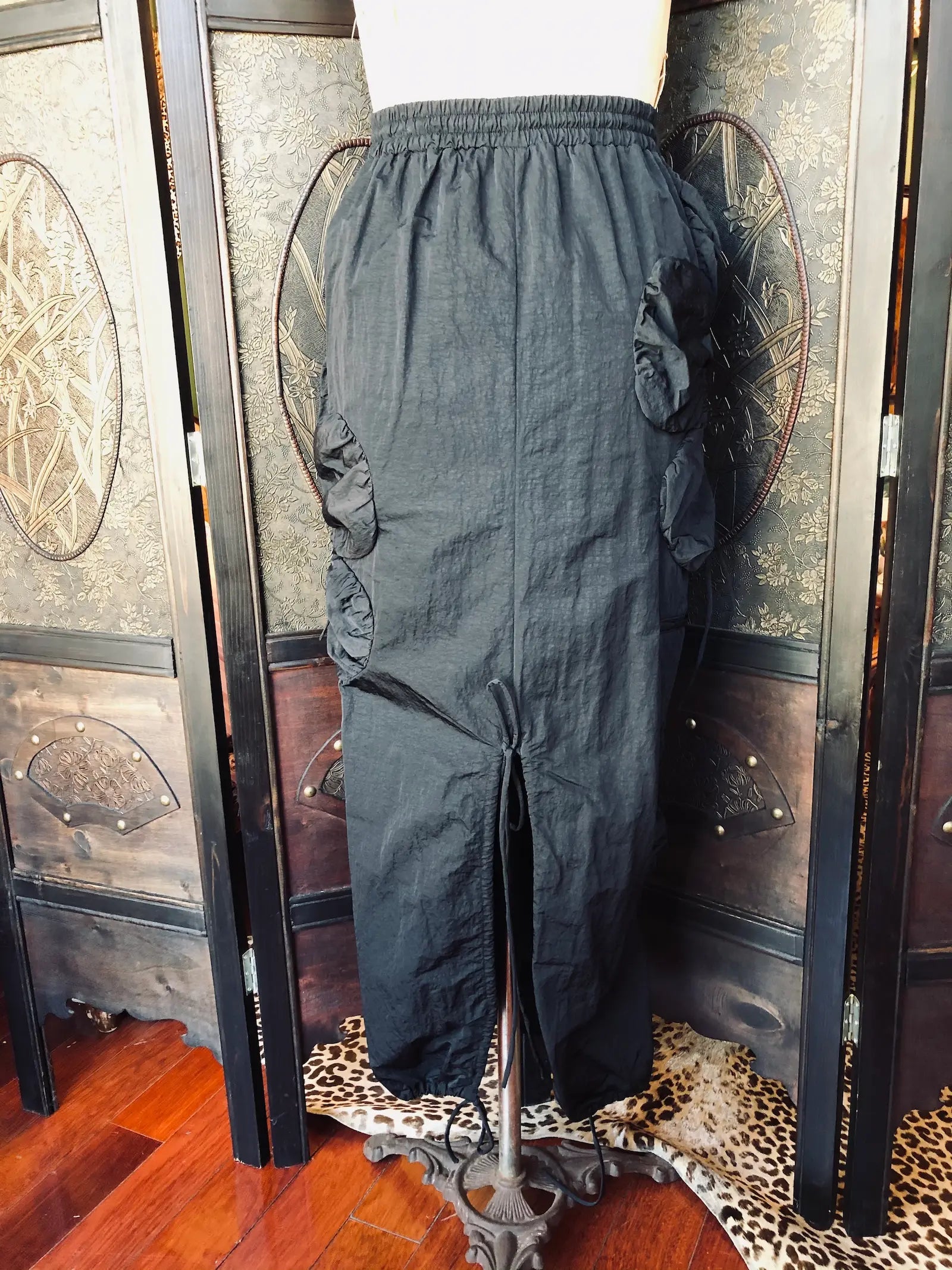 Broochella J Kim Small, 100% nylon, Black
Elasticated drawstring waist. Sculptural rosette appliqué detailing
Adjustable drawstring accents
Lightweight non stretch fabric. It is presented on a vintage mannequin. The background is a vintage, decorative, wooden room divider. 
